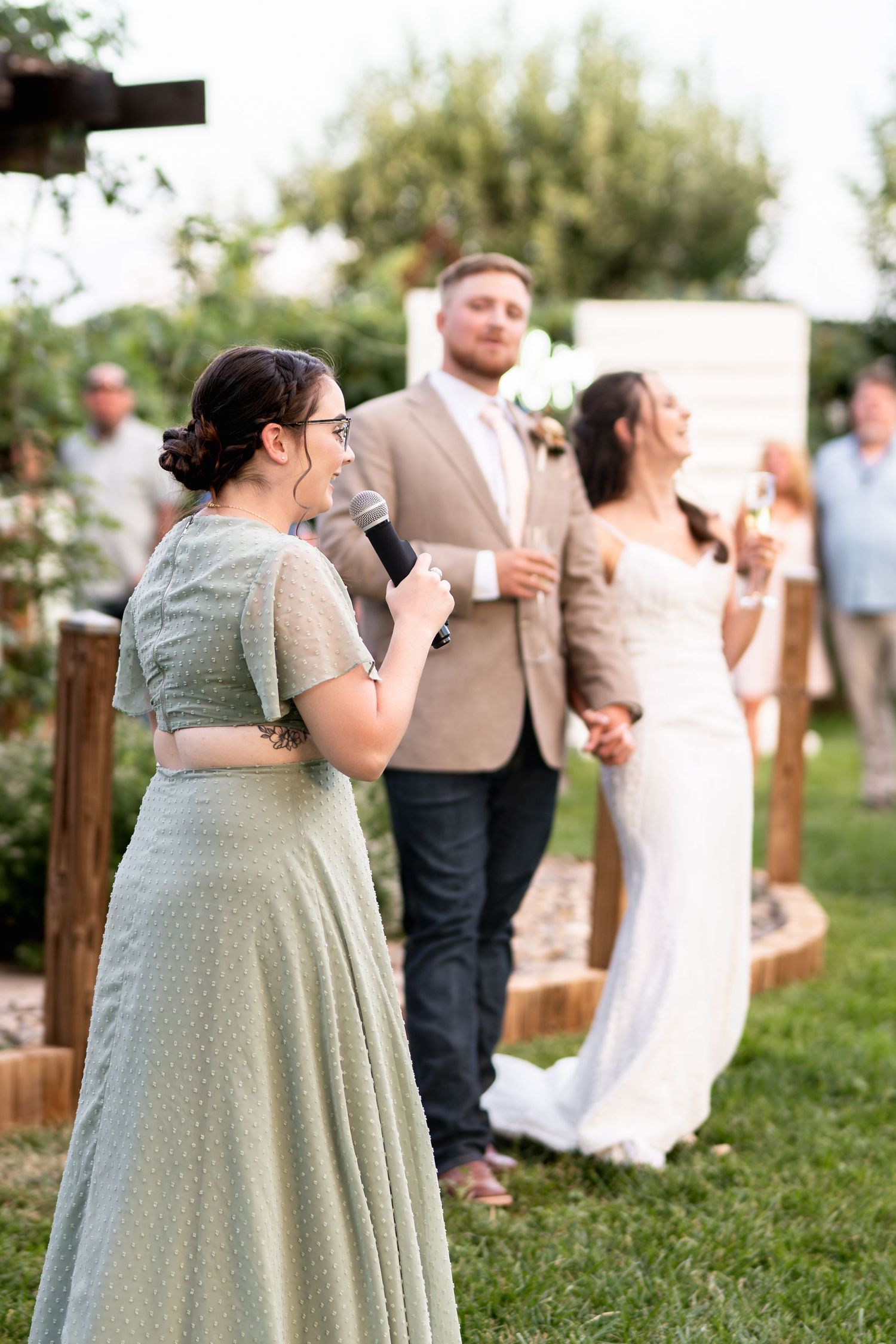 A wedding speech being given outdoors by a bridesmaid in a sage green dress.