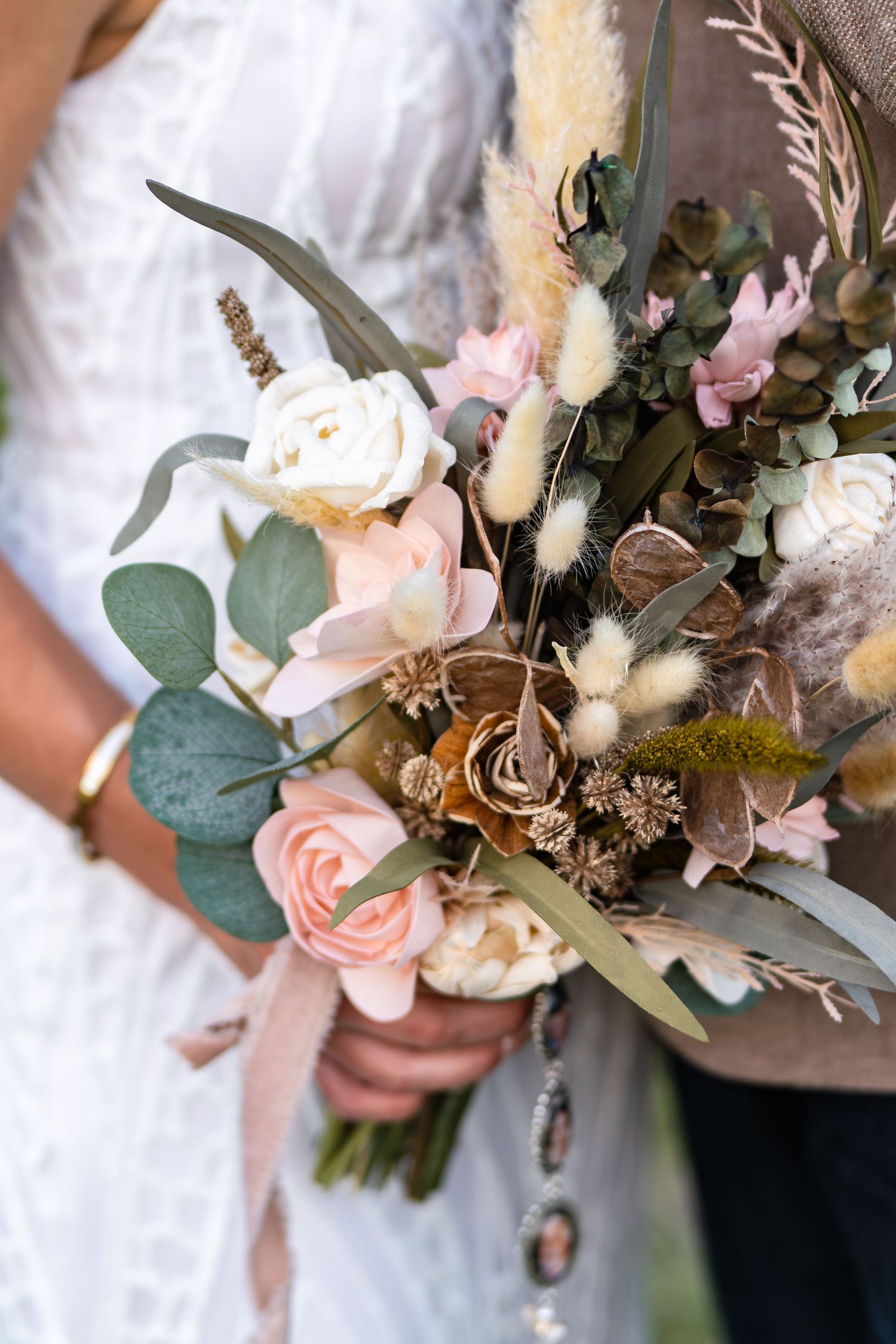 Close-up of boho wedding bouquet with roses, dried flowers, and eucalyptus in soft pink and cream tones.