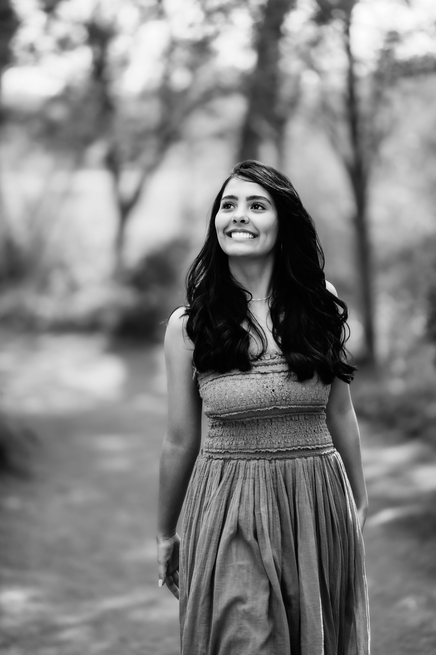 Black and white portrait of woman in flowing dress gazing upward with natural smile outdoors.