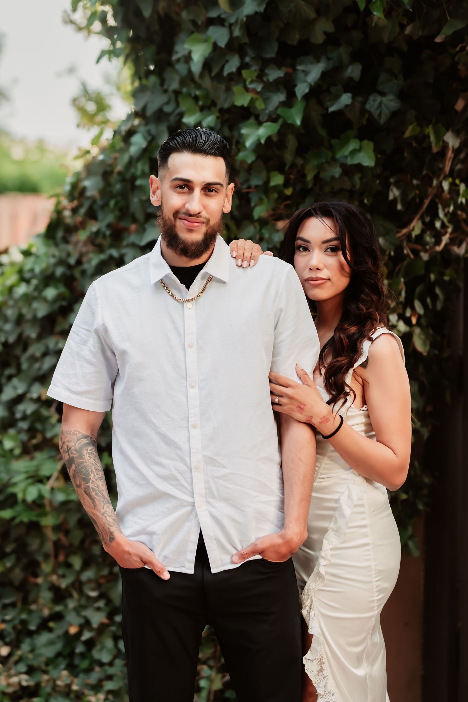 A romantic outdoor photoshoot featuring a couple in contrasting white and black outfits against a lush green backdrop.