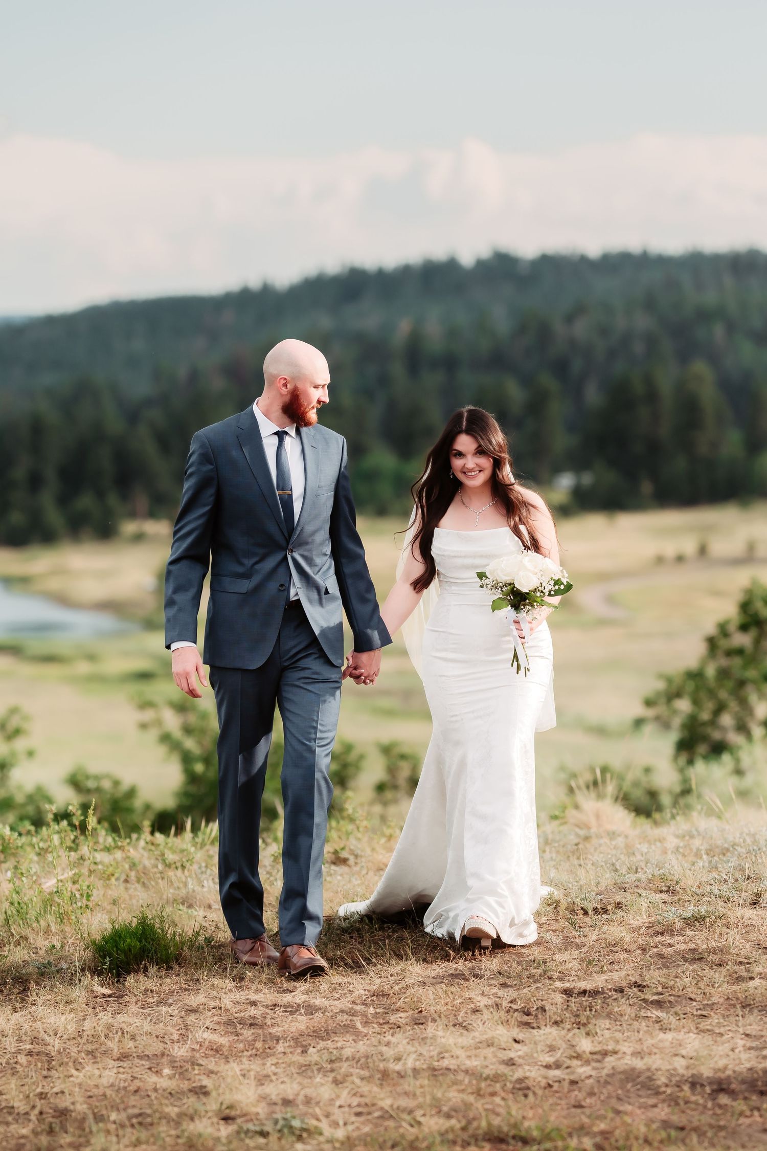Newlyweds walking hand in hand along a mountain ridge.