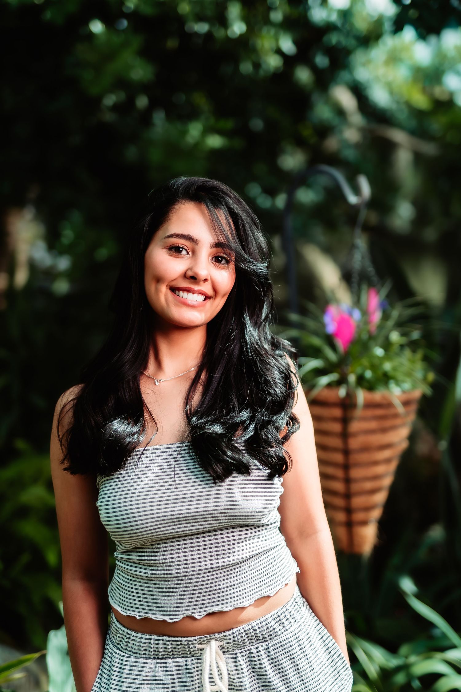 A portrait of someone wearing a striped crop top and matching pants while standing in a lush garden setting.