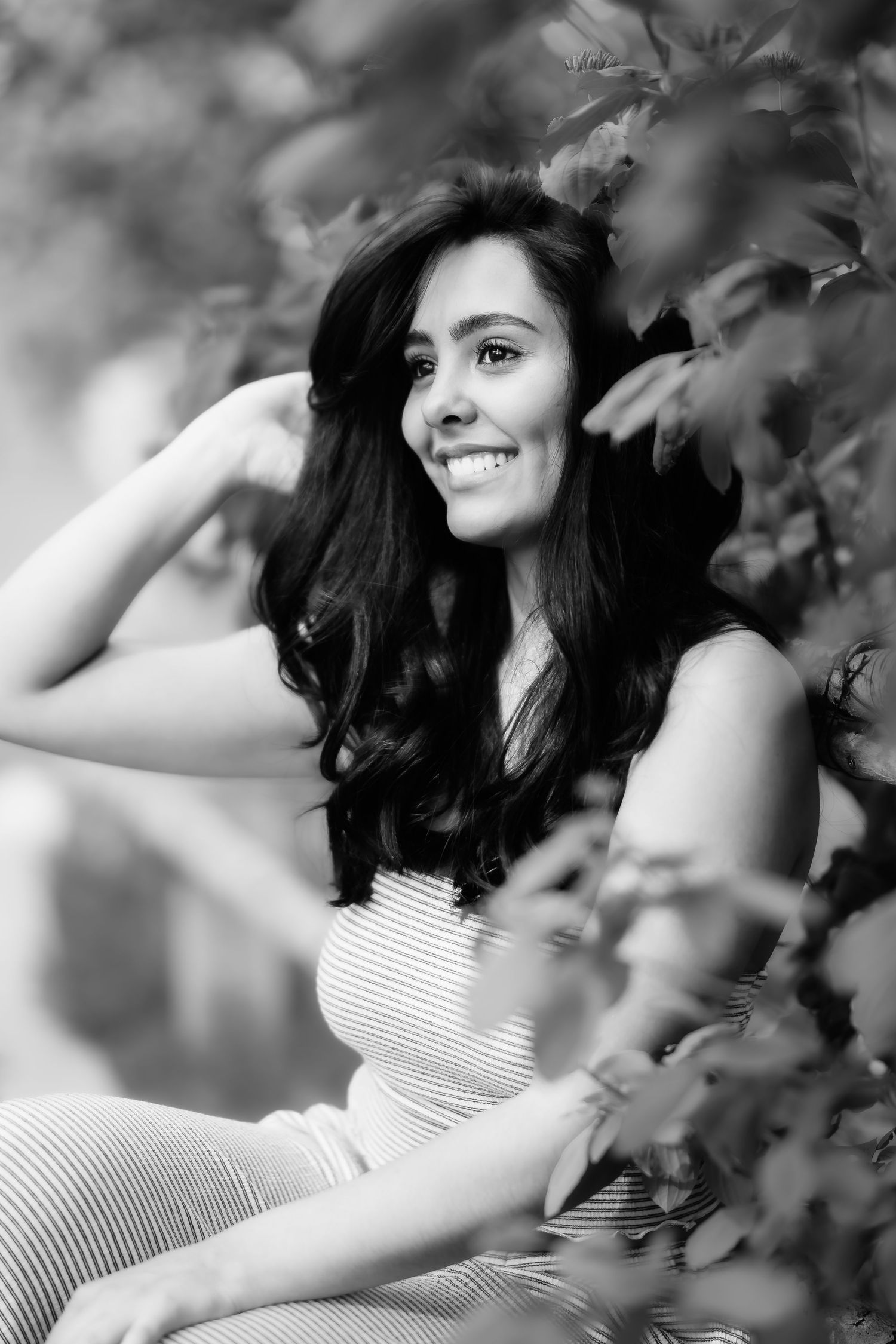 Black and white portrait of woman in striped dress surrounded by leaves.