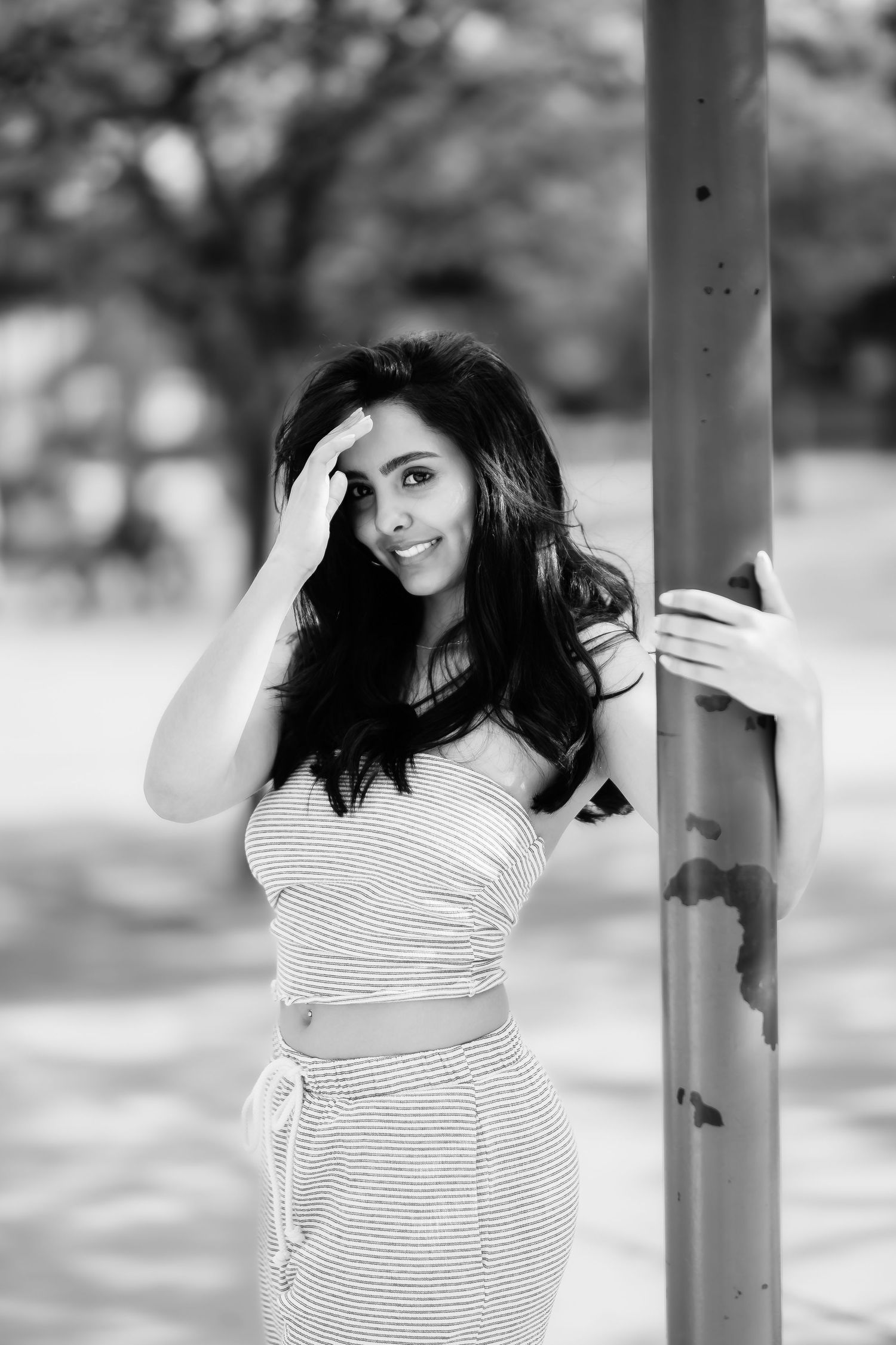 Black and white photo of a woman in striped dress leaning against a pole outdoors.