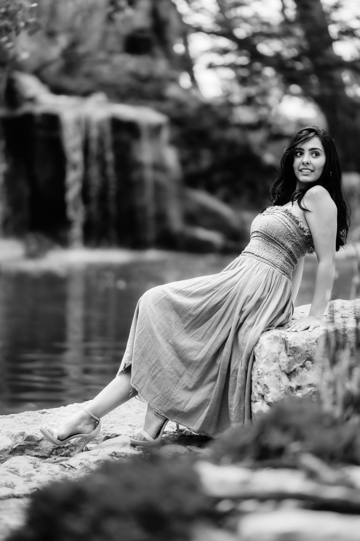 A black and white portrait by a waterfall showing elegant pose on rocks.