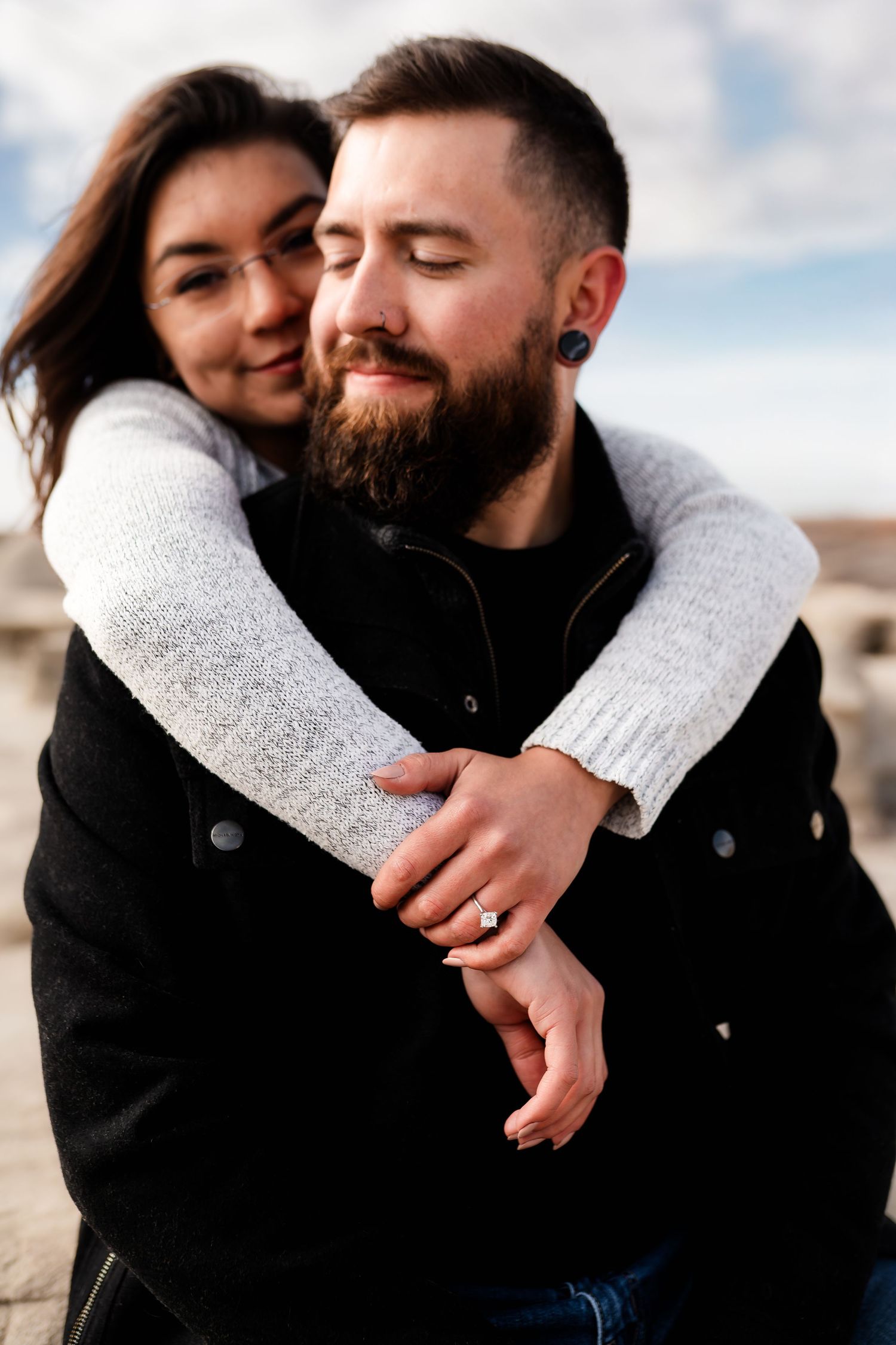 A couple embraces closely outdoors with desert rock formations in the background.
