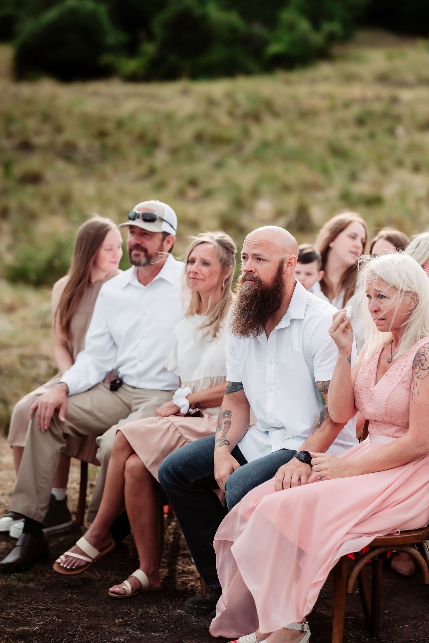 Wedding guests in pink dresses and white shirts seated outdoors for a ceremony.