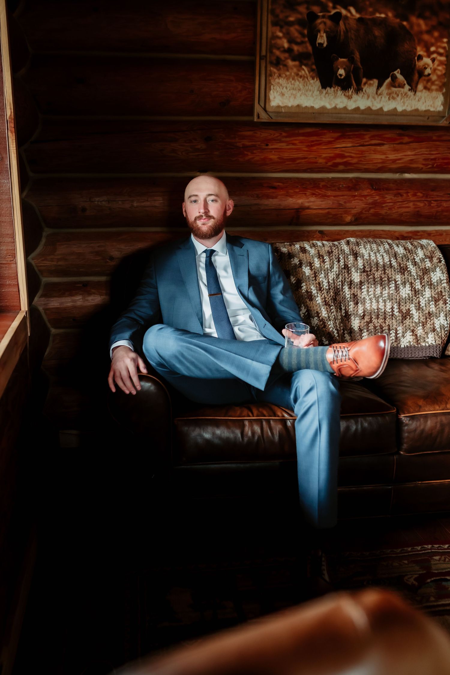 Portrait in blue suit relaxing on leather sofa with wooden cabin walls.
