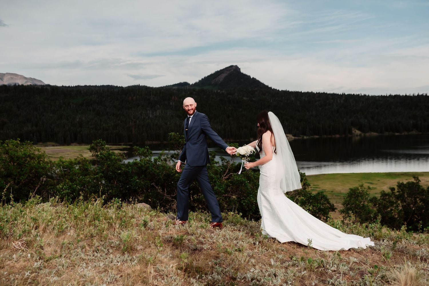 Wide angle view of a mountain wedding ceremony overlooking a scenic lake and forest.