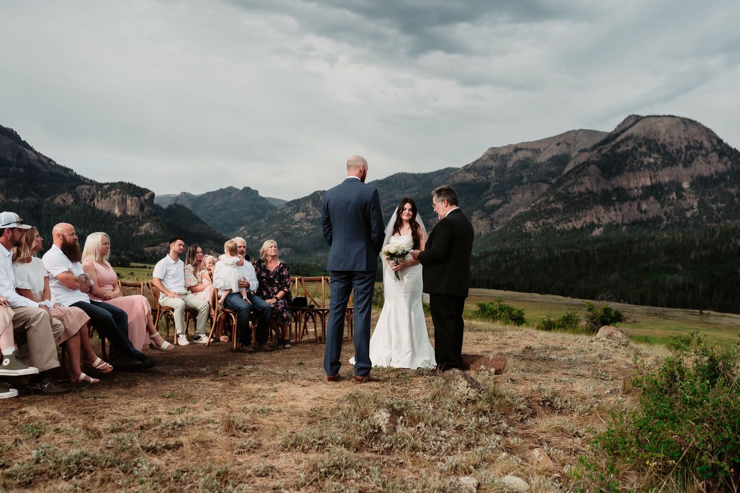An intimate outdoor wedding ceremony with guests seated facing majestic mountain views.