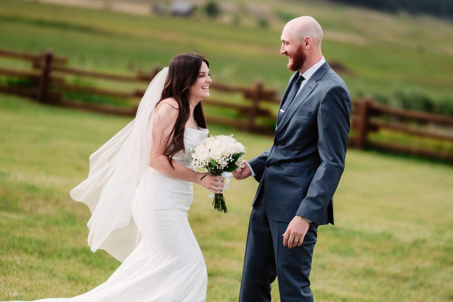 Wedding couple playfully interacting in an outdoor field with mountains in background.