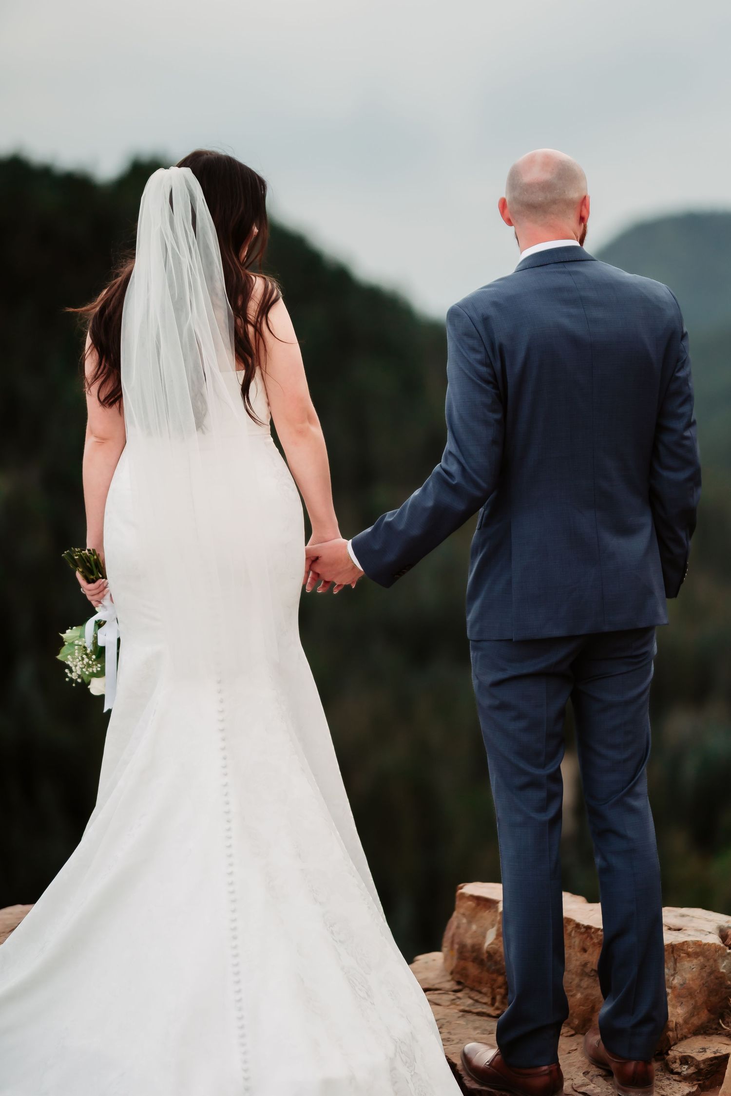 A couple walks hand in hand along a mountain ridge during their wedding photoshoot.