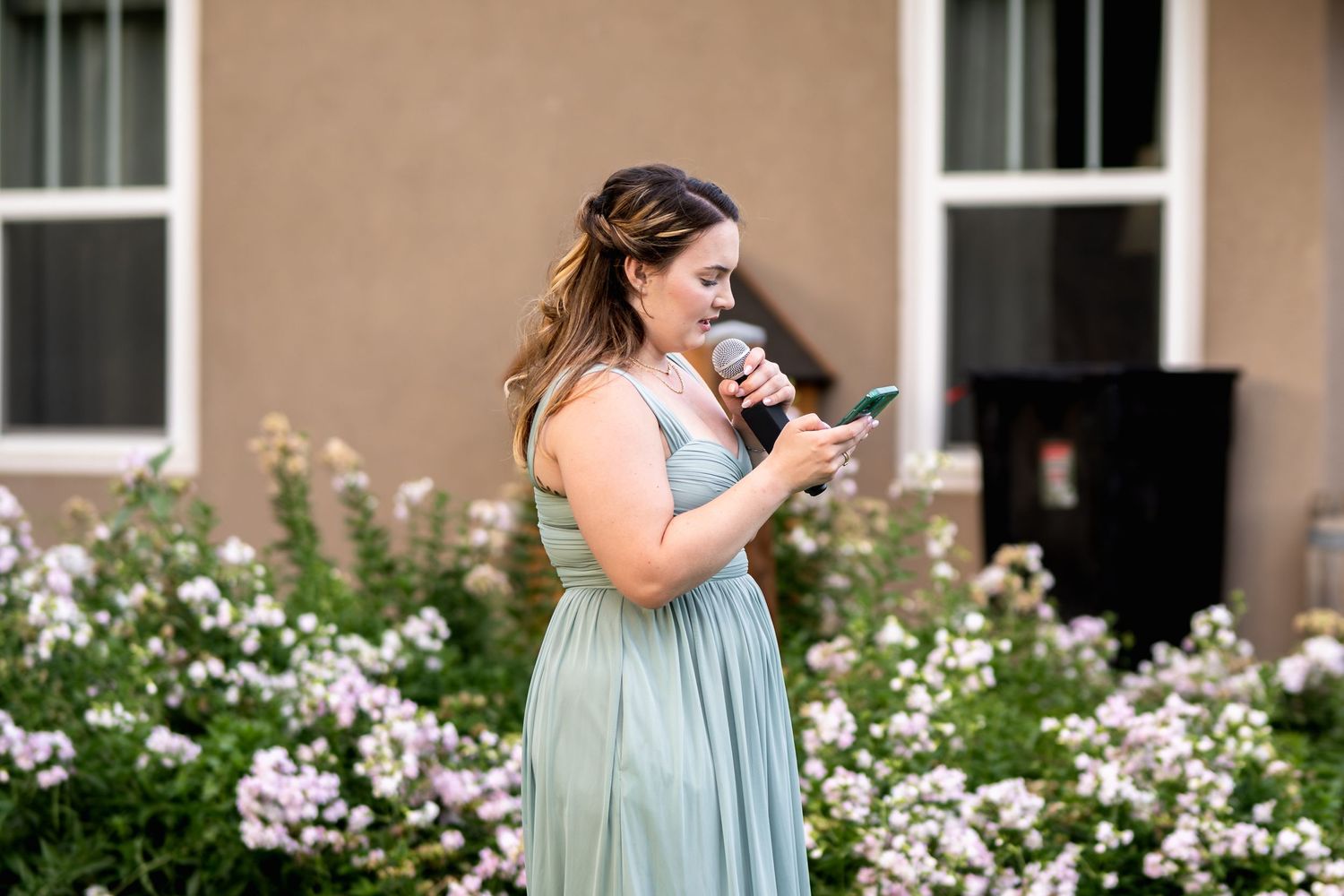 Bridesmaid in mint green dress stands among blooming garden flowers.