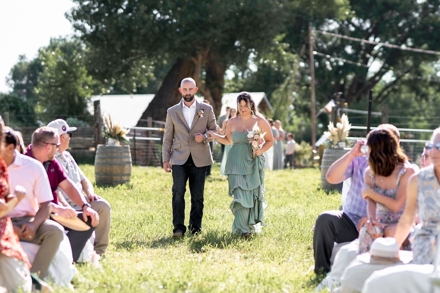 Wedding guests watch as a couple walks down the grassy outdoor aisle during a sunny summer ceremony.