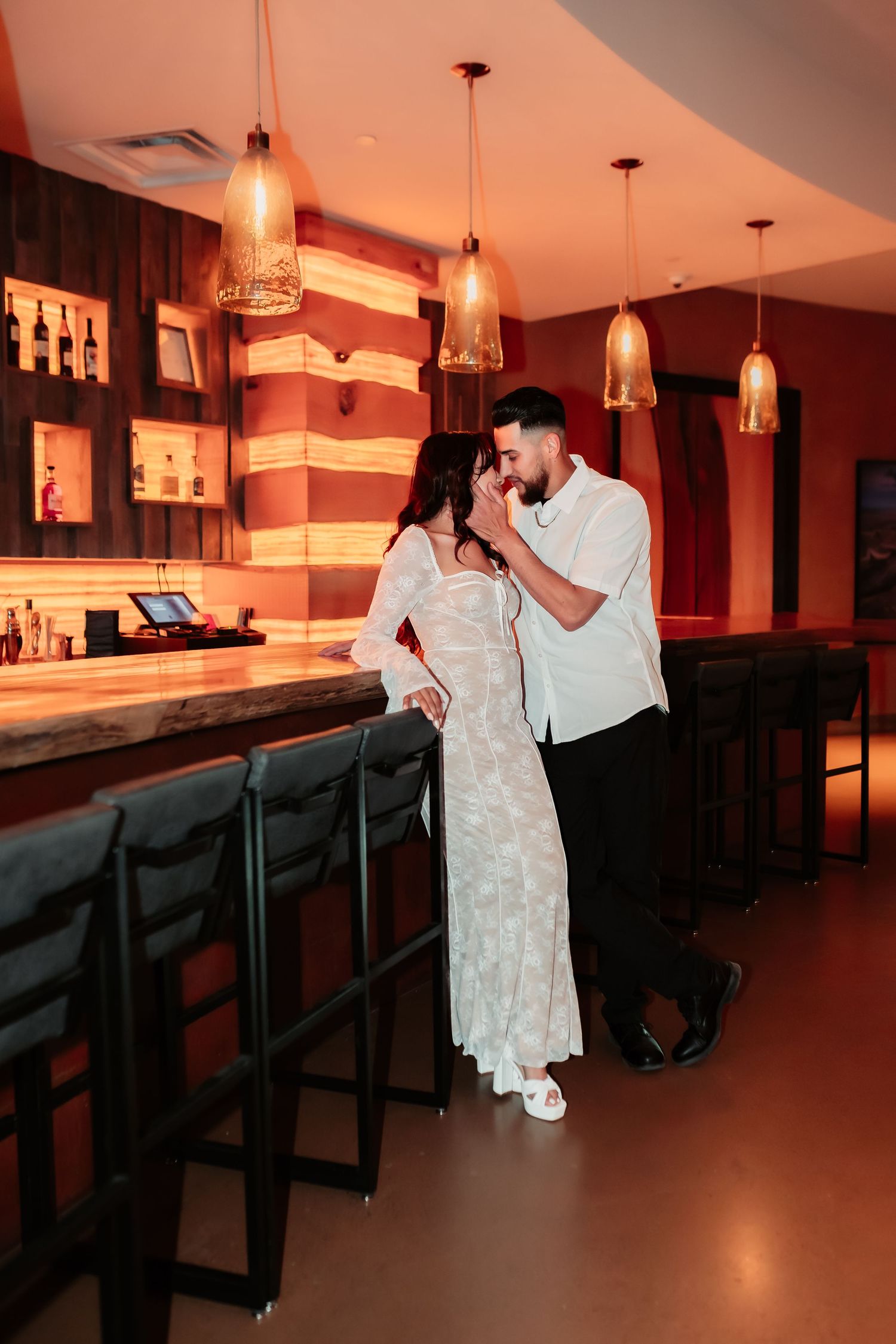 Stylish couple shares romantic moment at illuminated bar with pendant lighting.