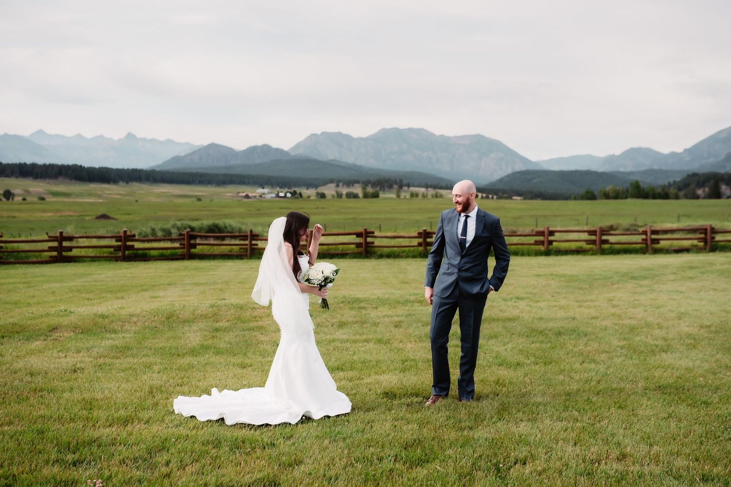 Wedding couple portraits in scenic mountain meadow with wooden fence in background.