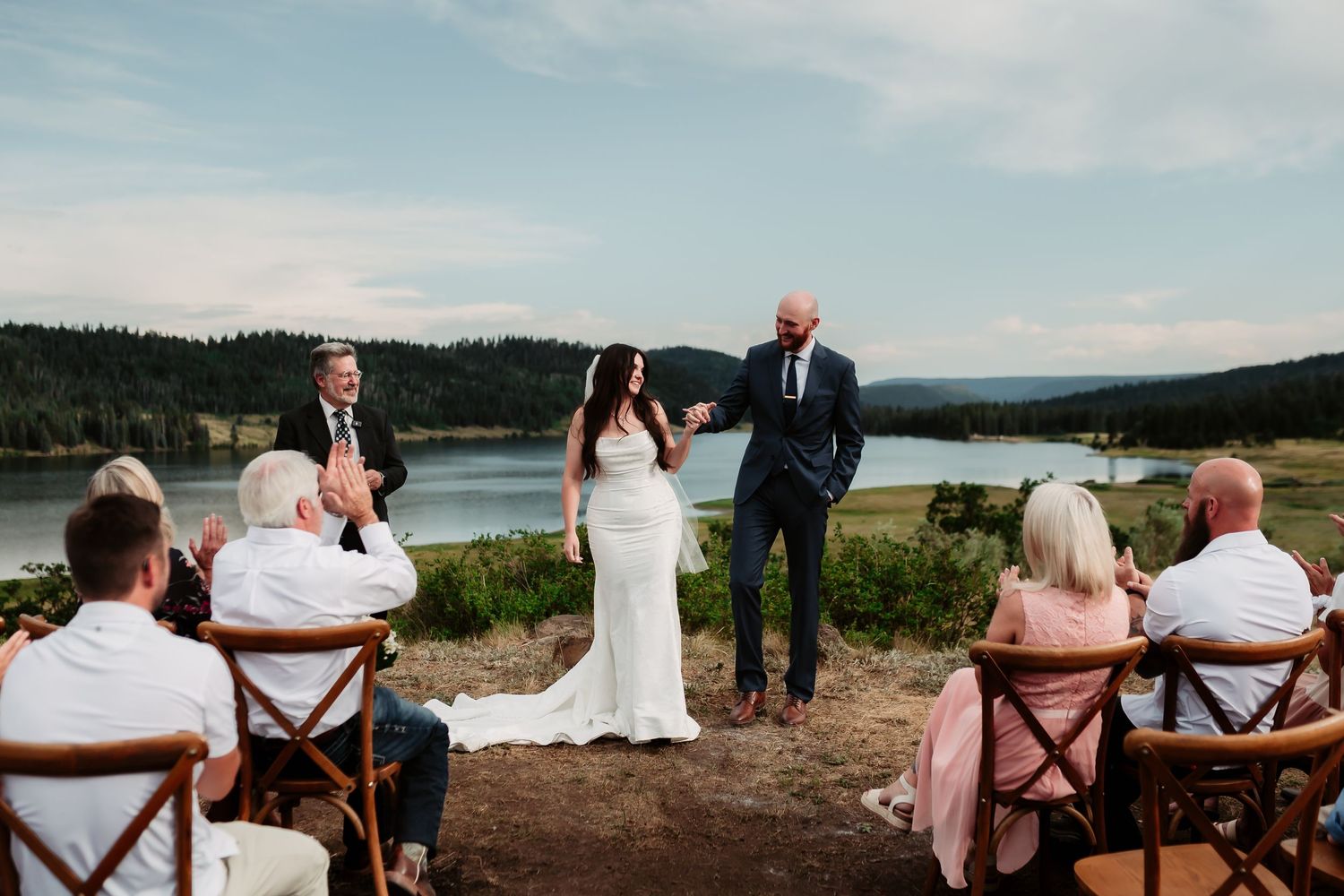 Wedding guests seated in wooden chairs at outdoor ceremony with mountain views.