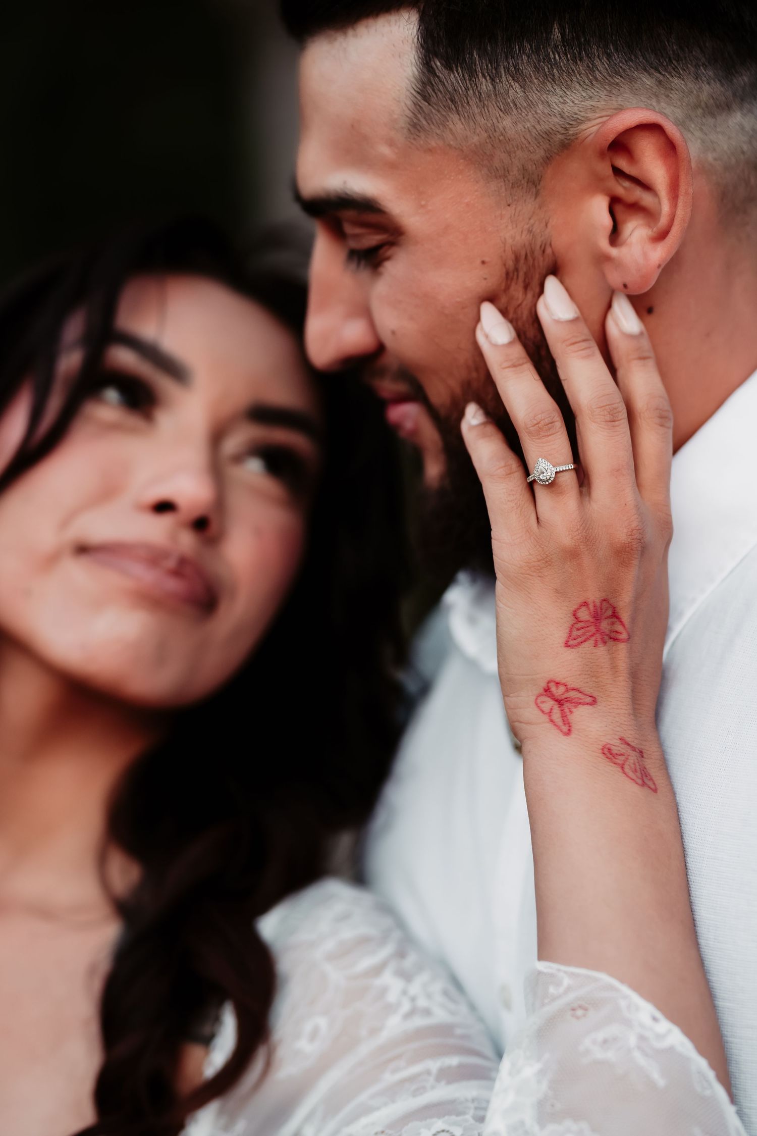 Close-up portrait showing affectionate moment between couple with visible butterfly tattoo and ring.