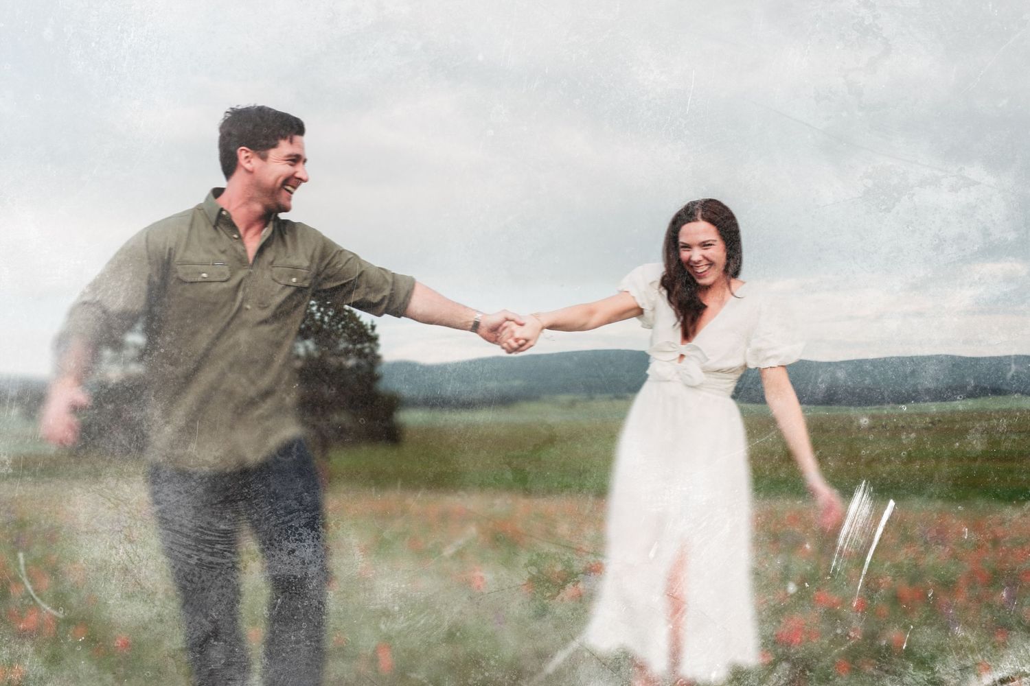 Couple sharing a romantic dance in a field of red poppies with mountains in the background on an overcast day.