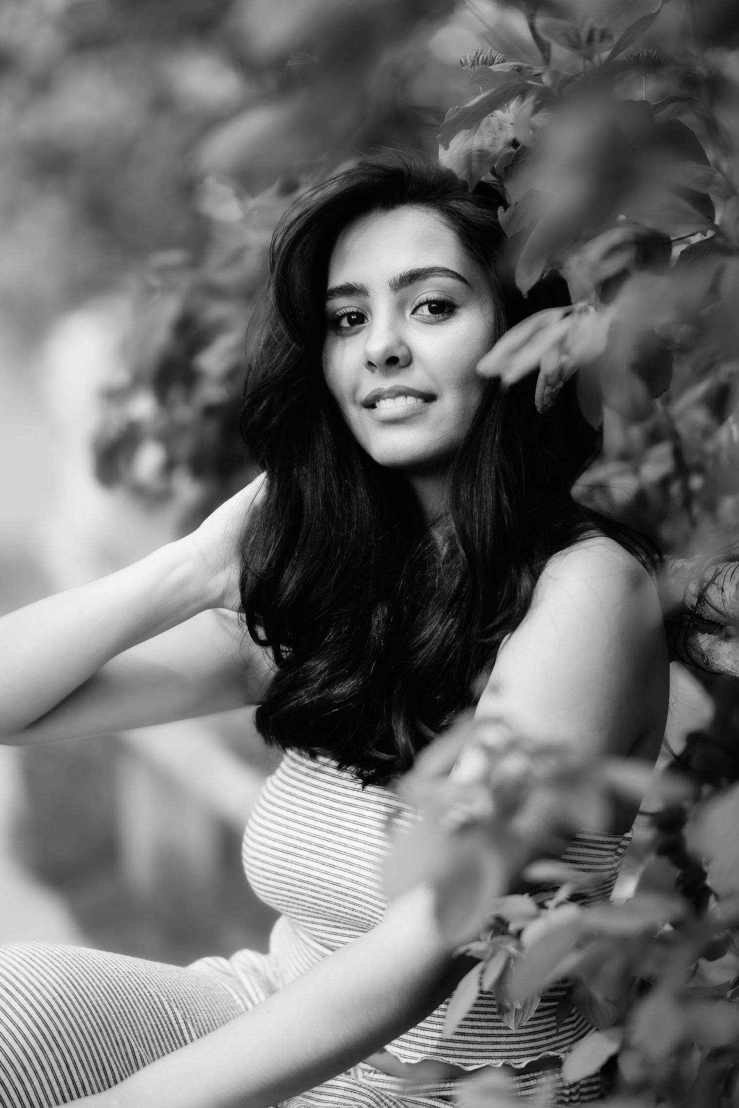 Black and white portrait of a woman in a striped dress posing outdoors among foliage.