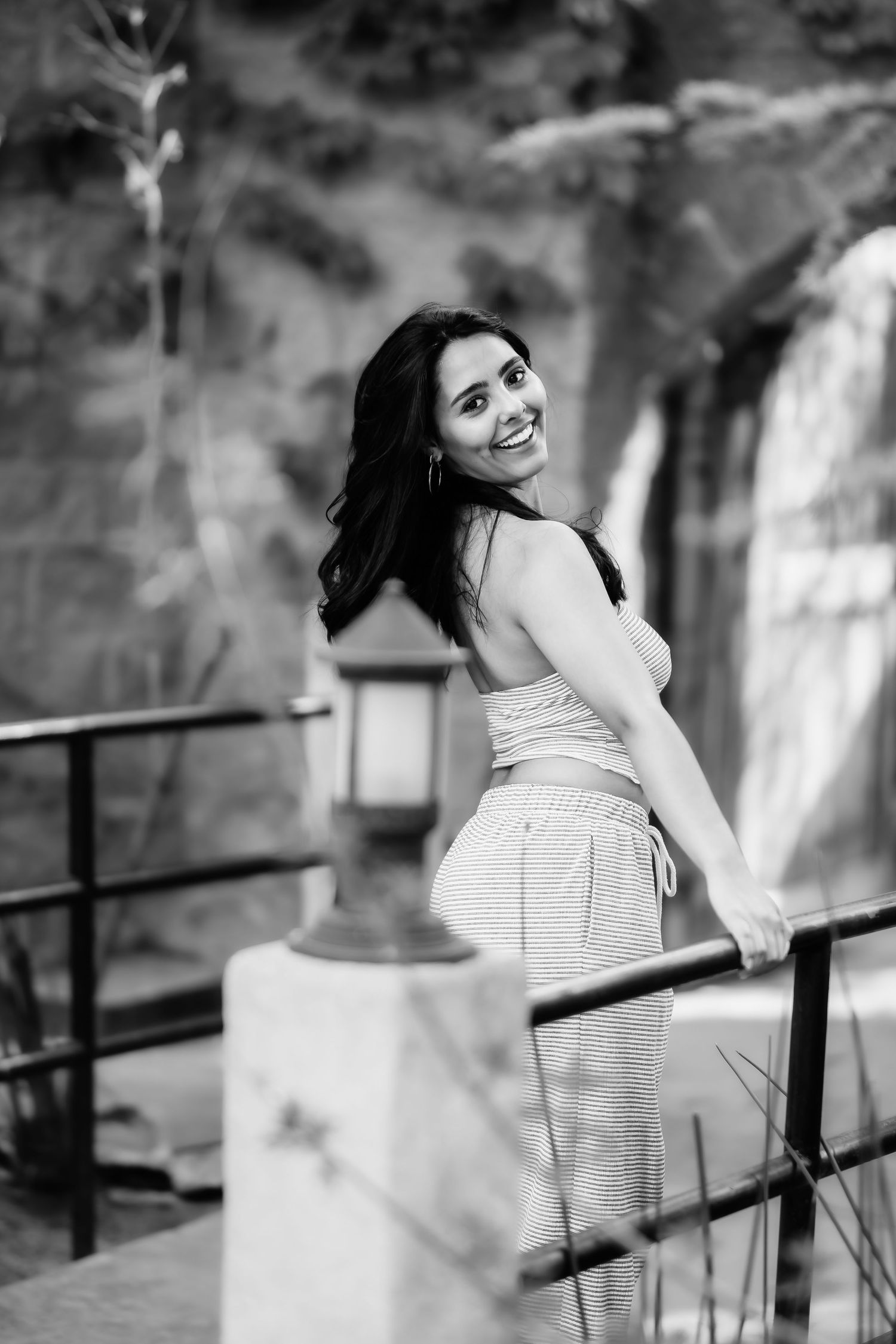 Woman in casual outfit smiles over shoulder while holding railing in black and white photo.