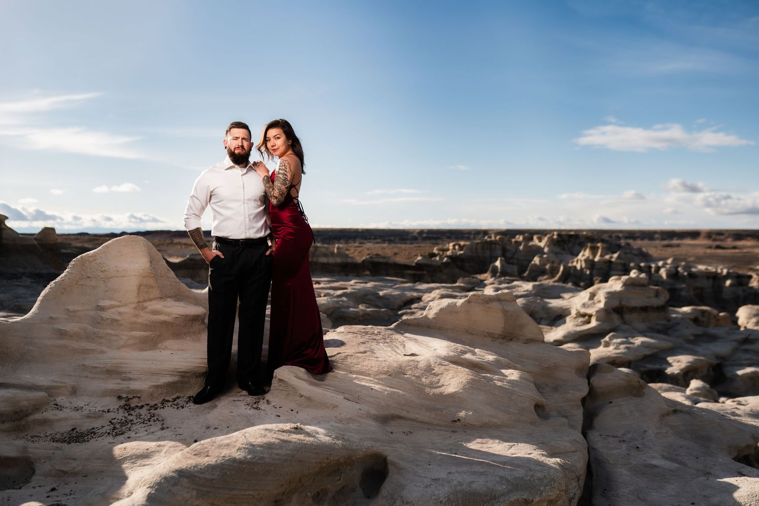 Couple stands together on unique rocky terrain under blue sky during outdoor desert photoshoot.