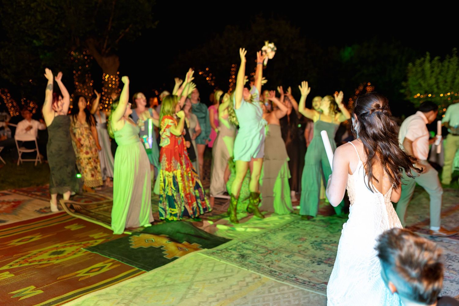 Wedding guests dancing and celebrating on illuminated outdoor dance floor.