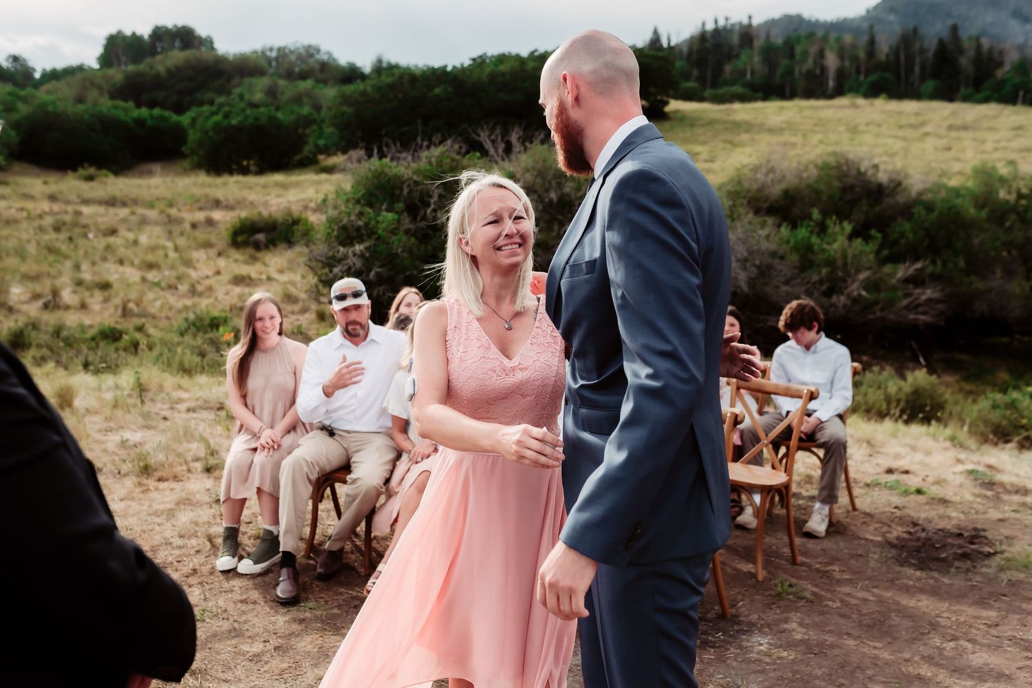 Wedding celebration moment with guests seated outdoors against mountain backdrop.
