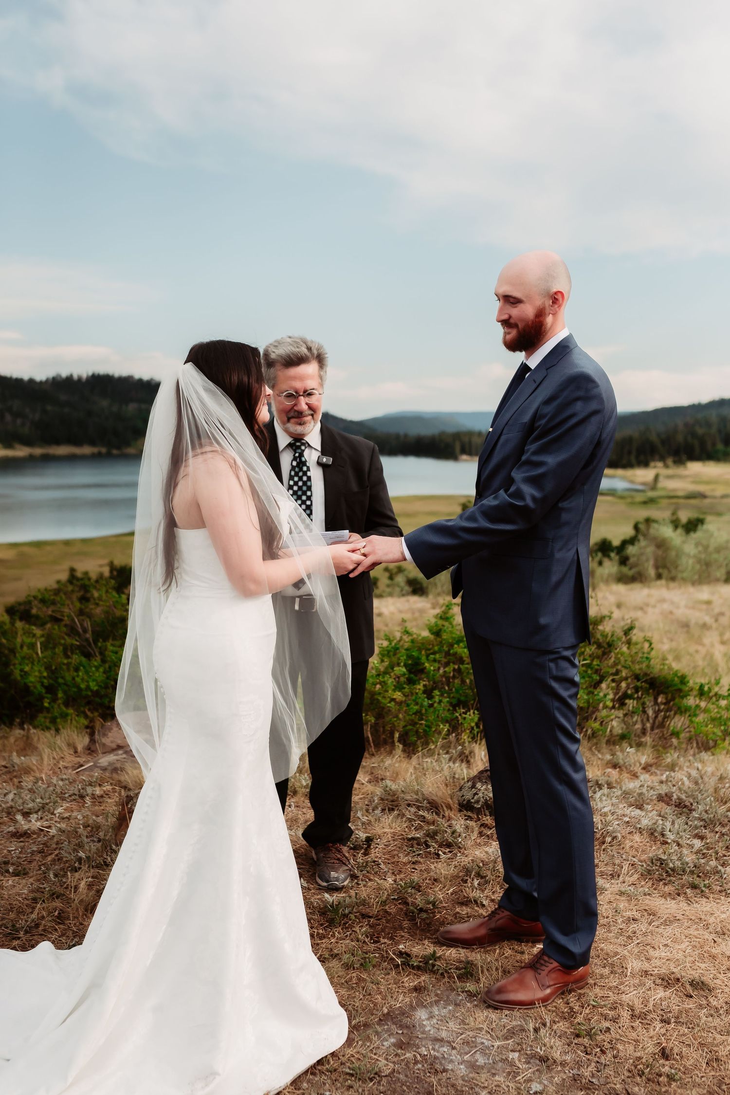 A scenic mountain wedding ceremony with a couple exchanging rings overlooking a serene lake.