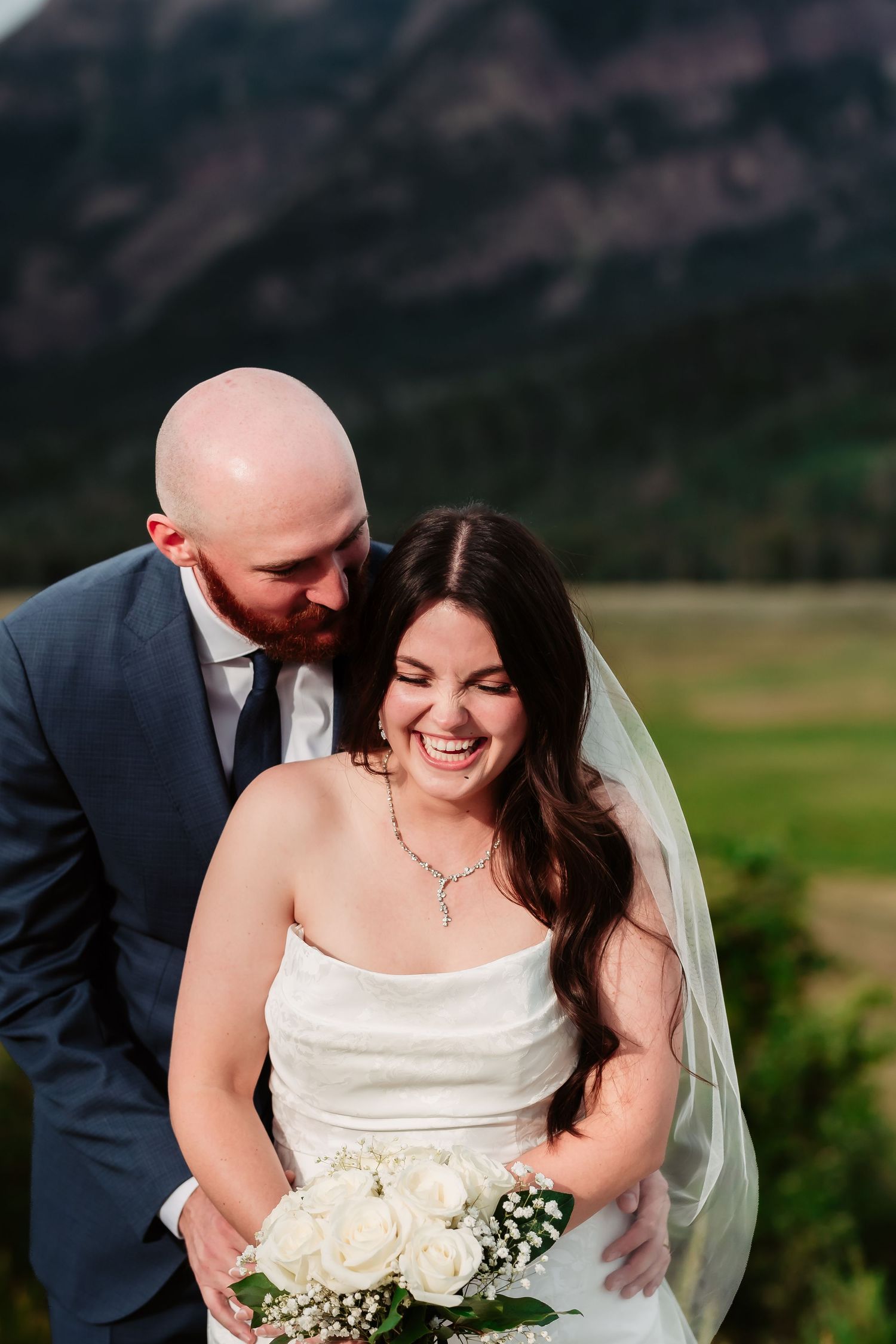 A romantic wedding portrait captured against the backdrop of mountains and green fields.