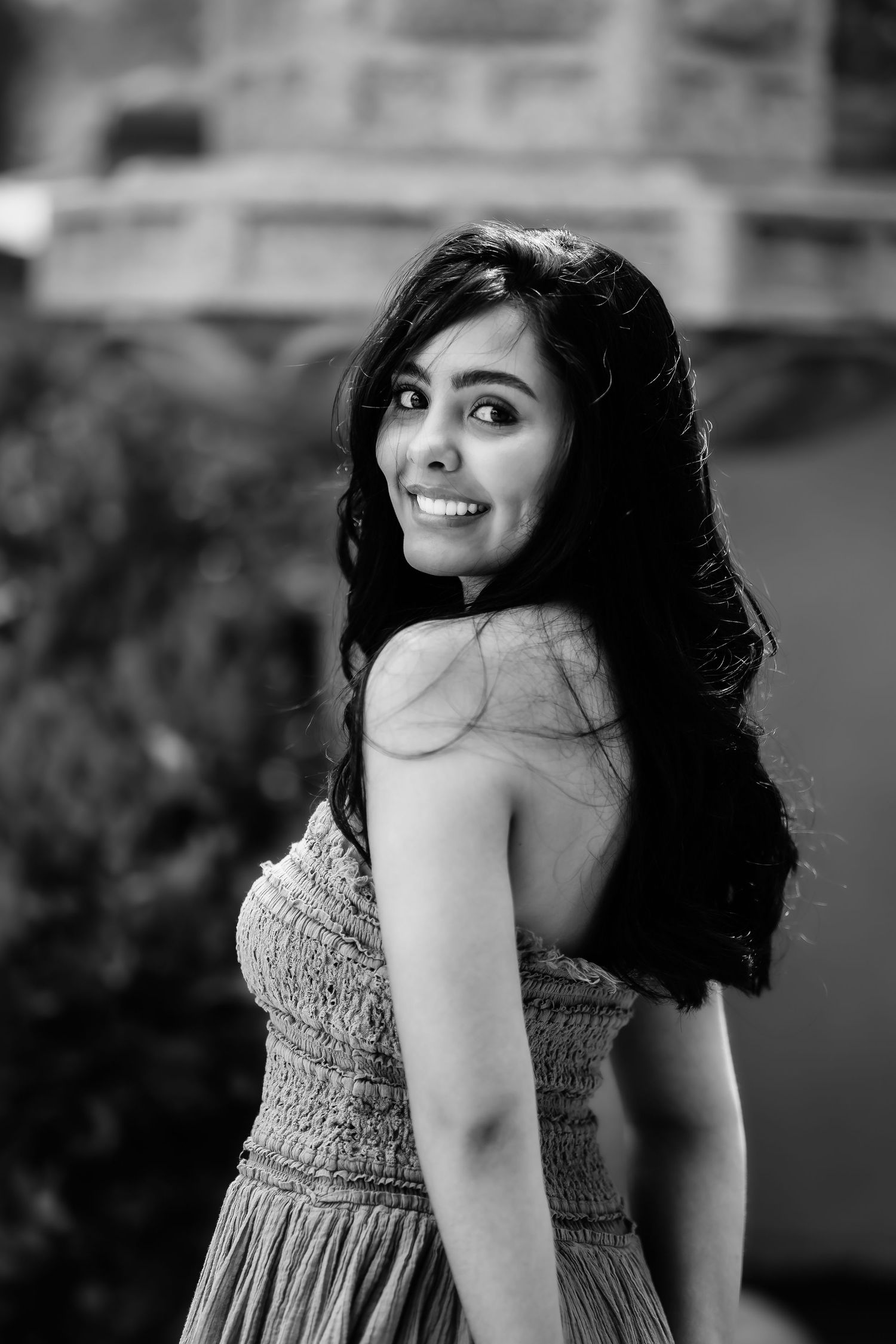 Black and white portrait of woman in textured dress with flowing dark hair and radiant smile.