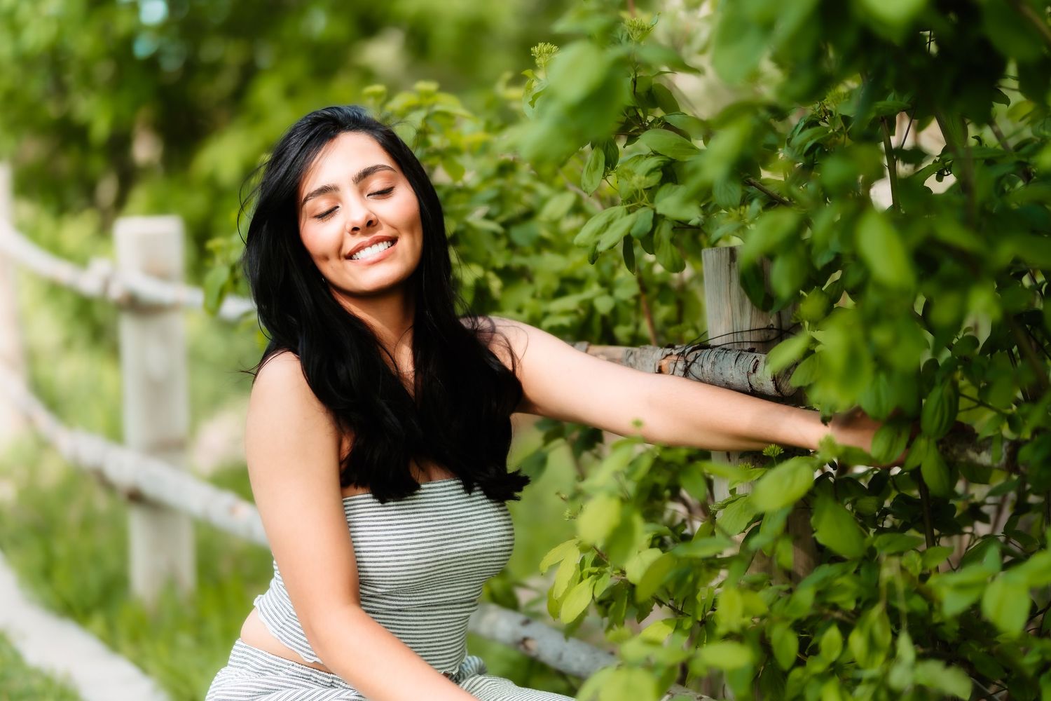 Candid shot of someone reaching towards green leaves while wearing a gray outfit.