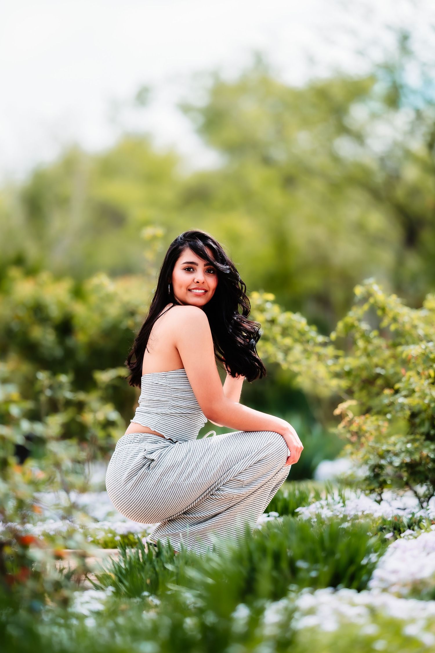 Someone poses in a gray outfit among blooming wildflowers in a garden setting.