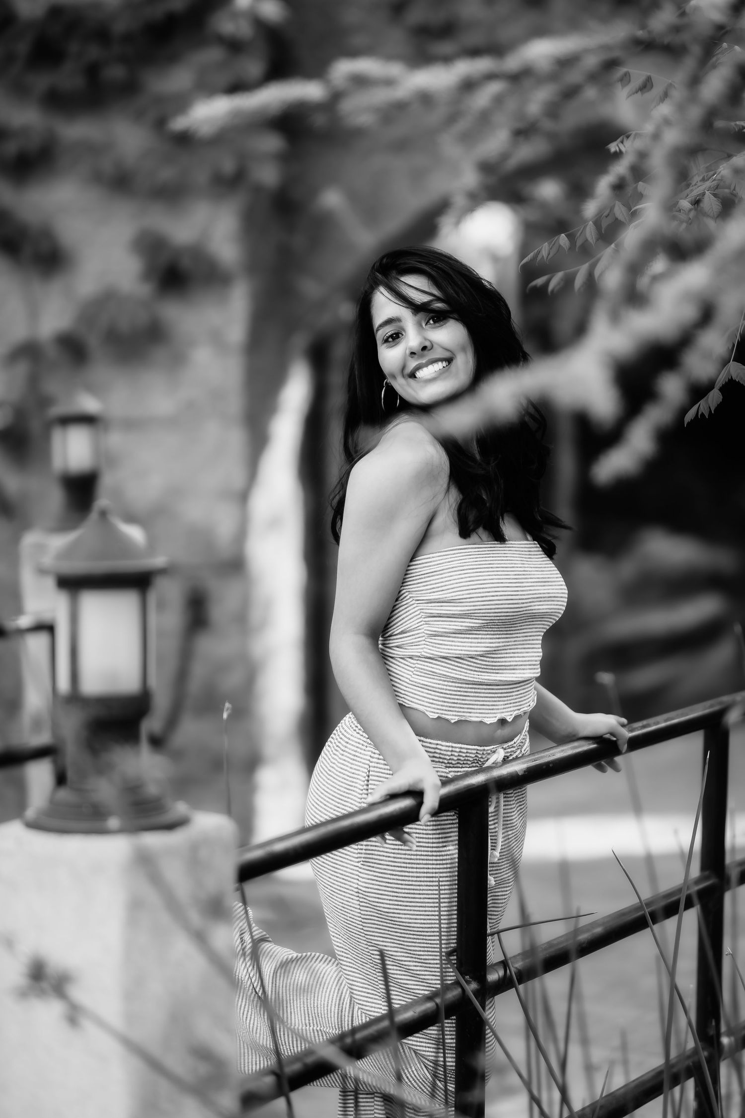 A black and white portrait shows someone smiling while leaning on a railing with lanterns in the background.