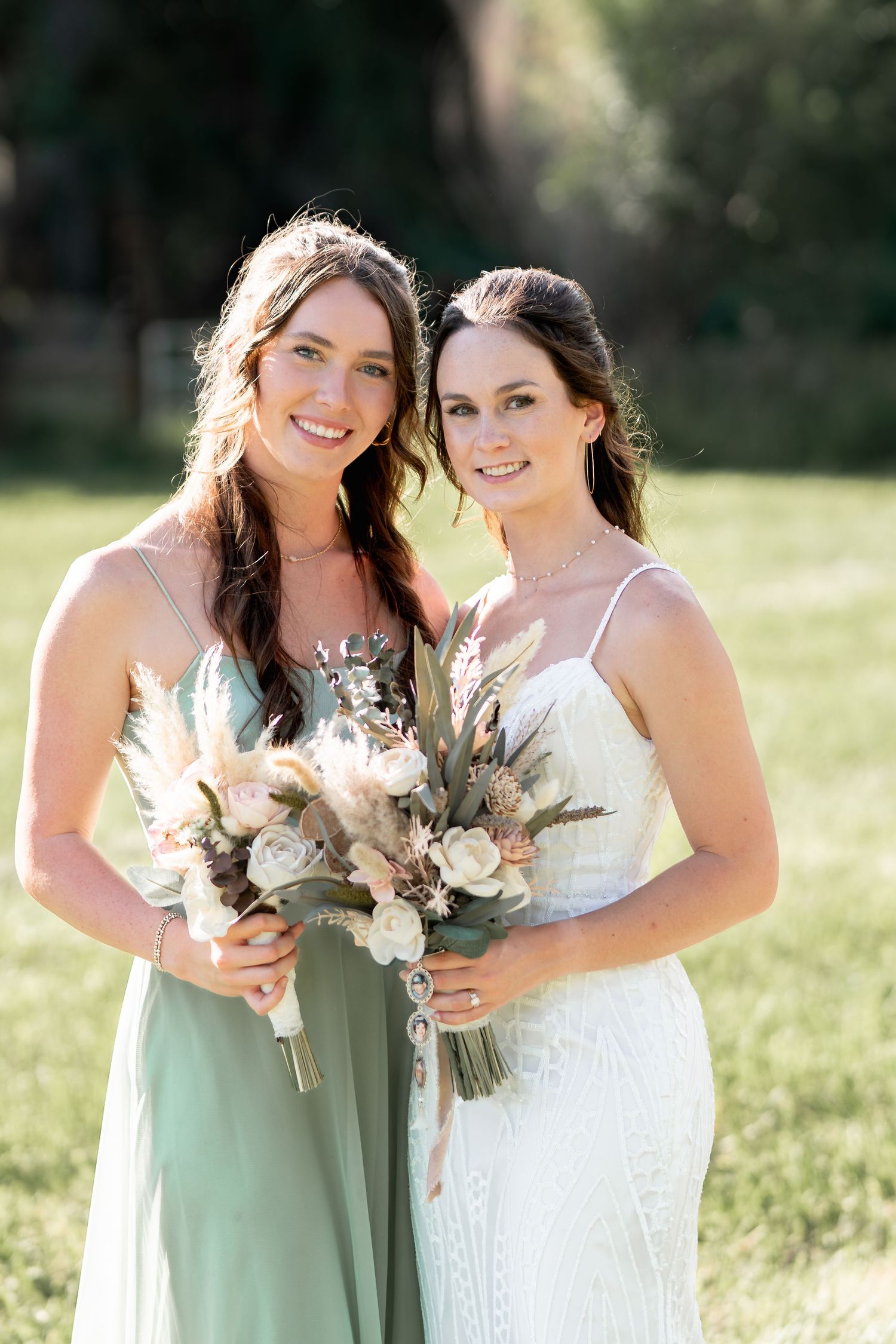 Wedding party members hold matching bouquets of roses and dried flowers in outdoor setting.