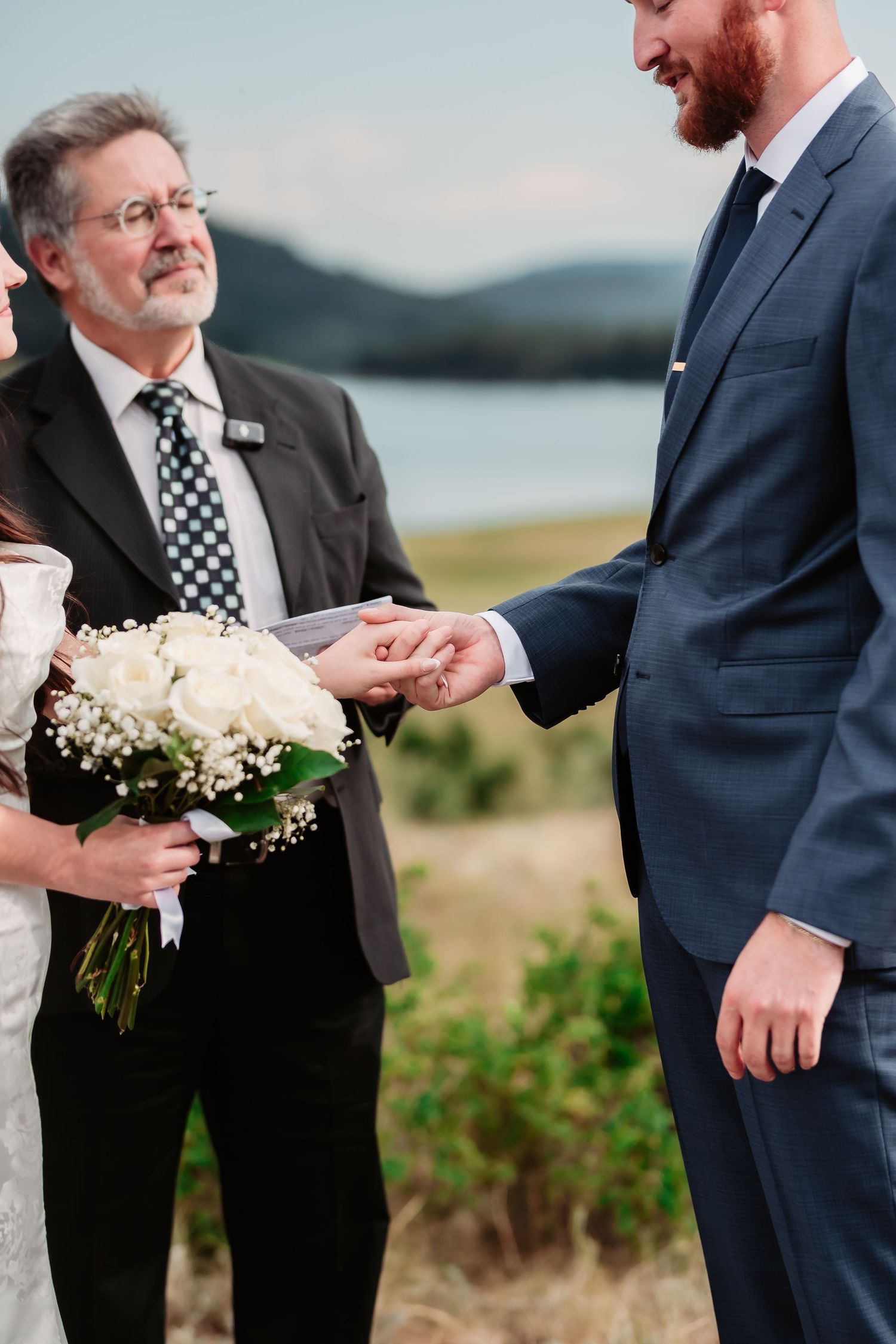 A touching moment during a lakeside wedding ceremony with white floral bouquet details.