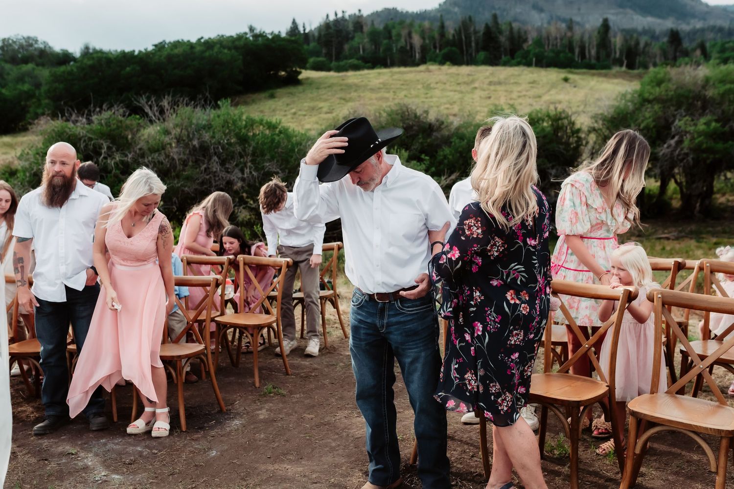 Wedding guests seated in wooden chairs on a scenic hillside overlooking mountains.