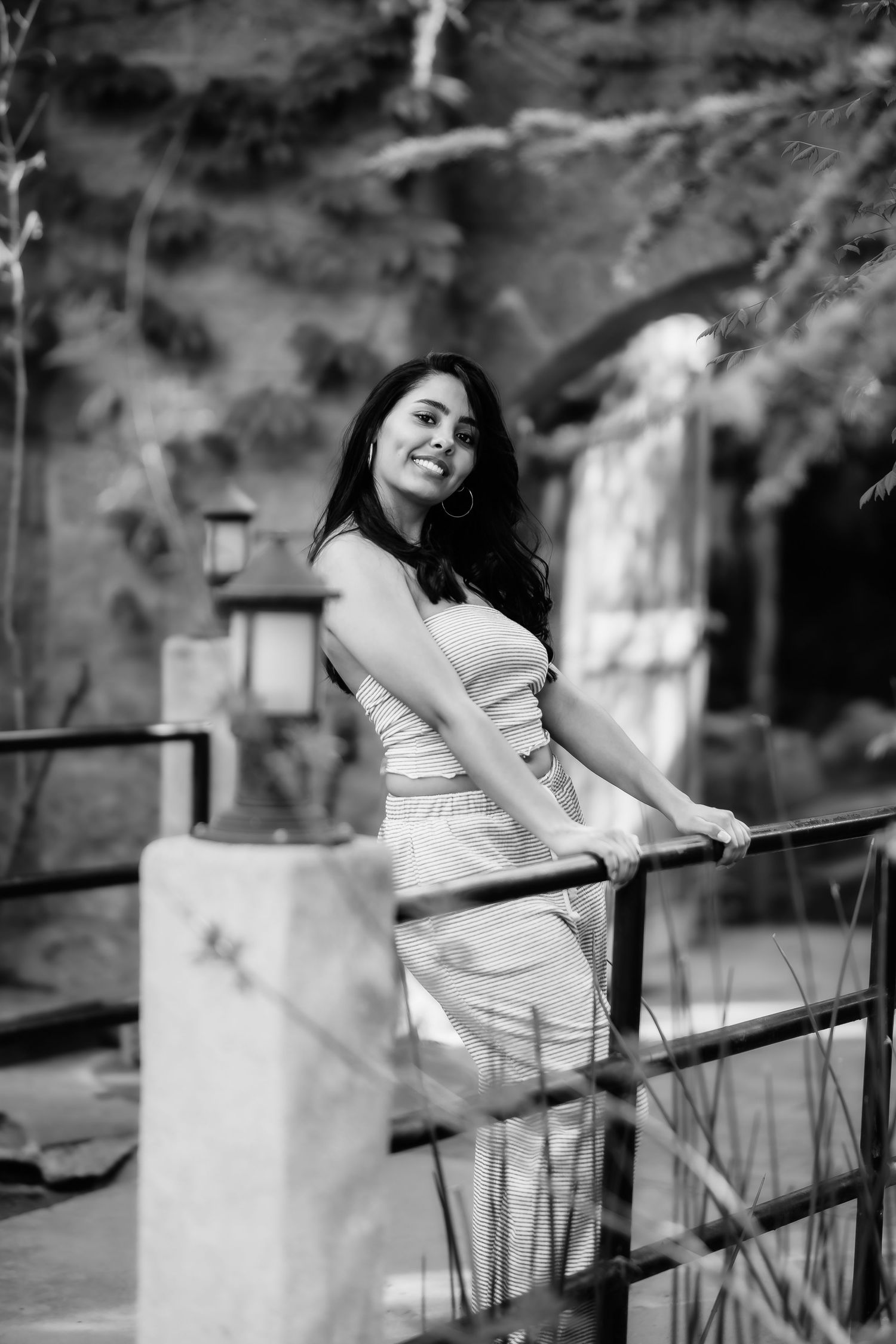 Black and white image of a woman in light clothing leaning on an outdoor railing near lanterns.