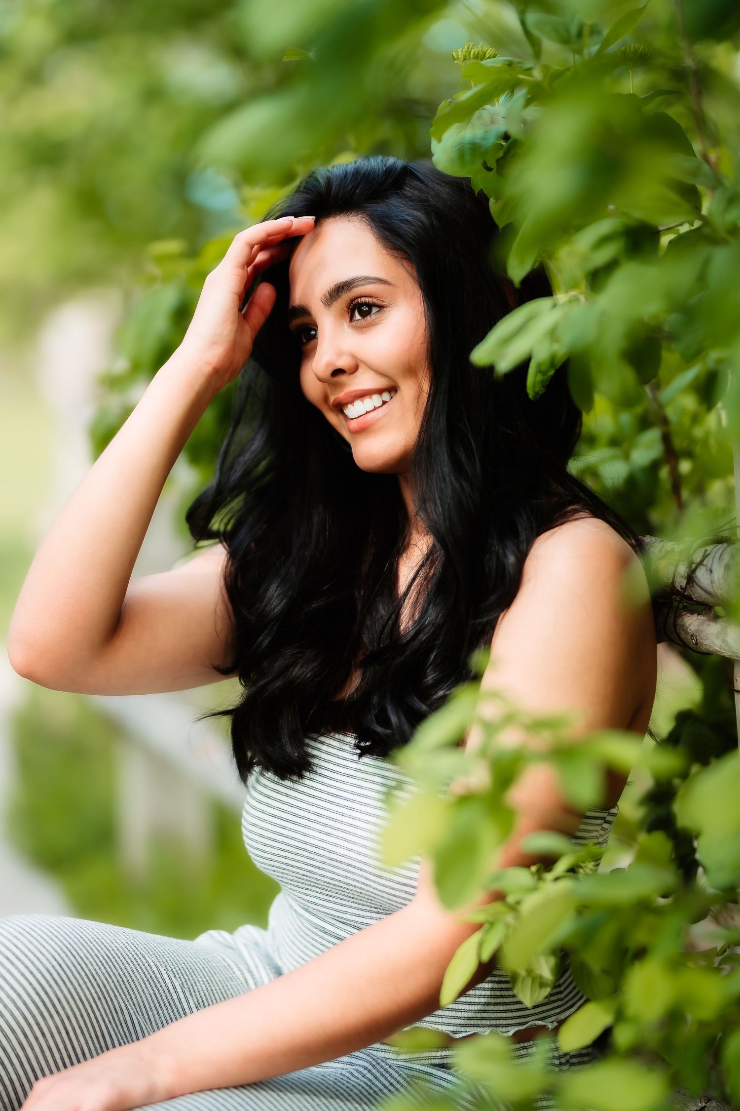 Natural outdoor portrait with long dark hair framed by green leaves.