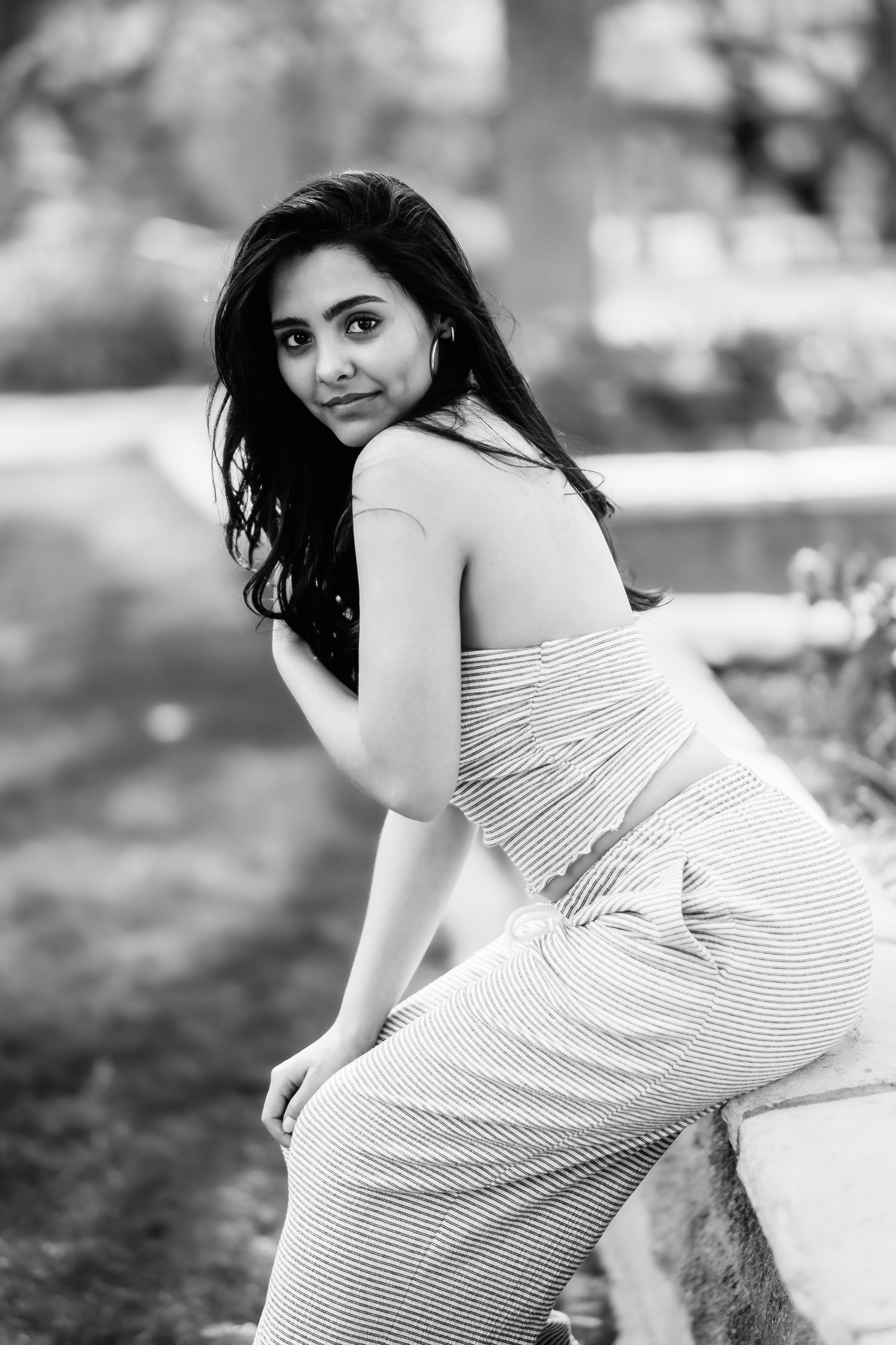 Black and white portrait of a woman in fitted striped dress posing by a garden wall.