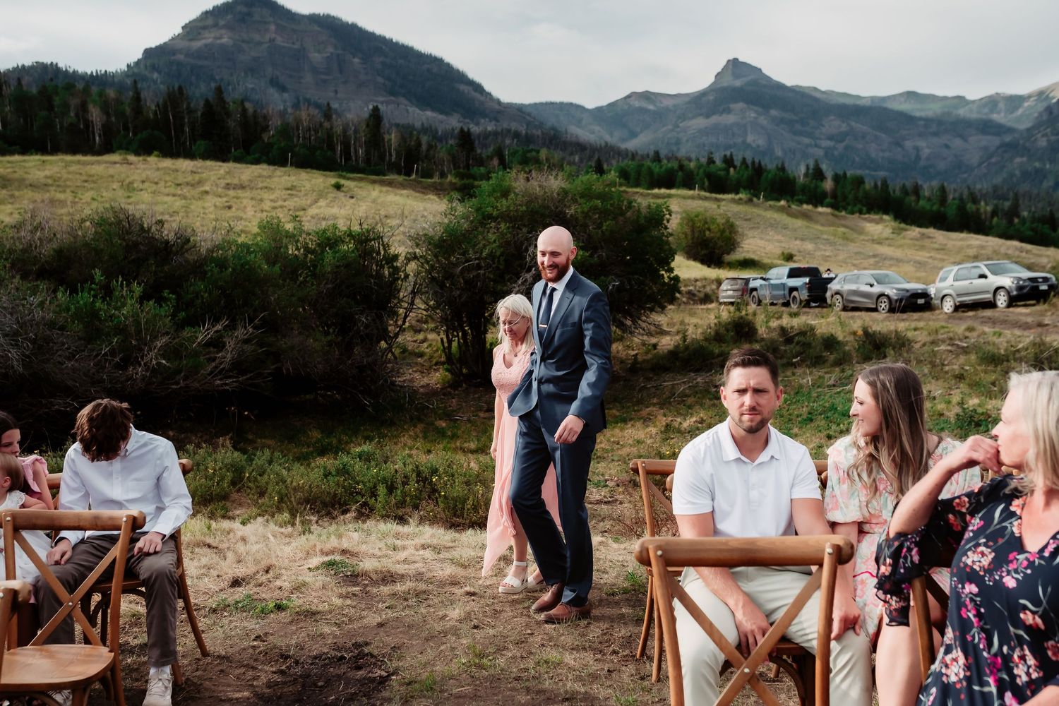 Panoramic mountain landscape with wedding guests gathered for an outdoor ceremony.