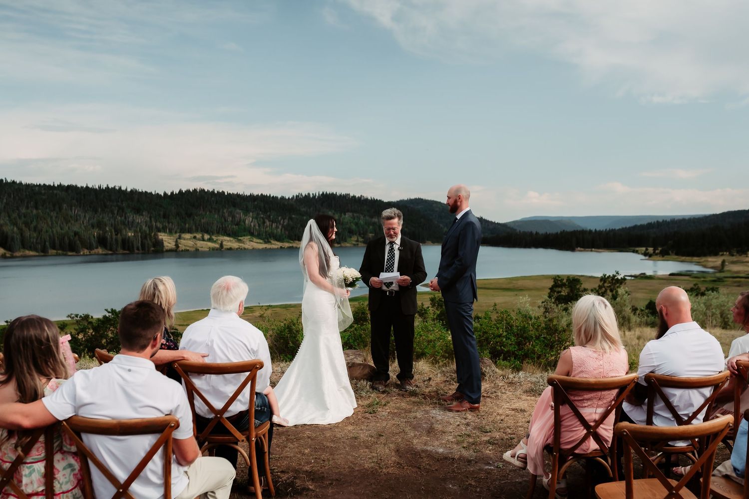 An intimate lakeside wedding ceremony with mountain views and wooden chairs for guests.