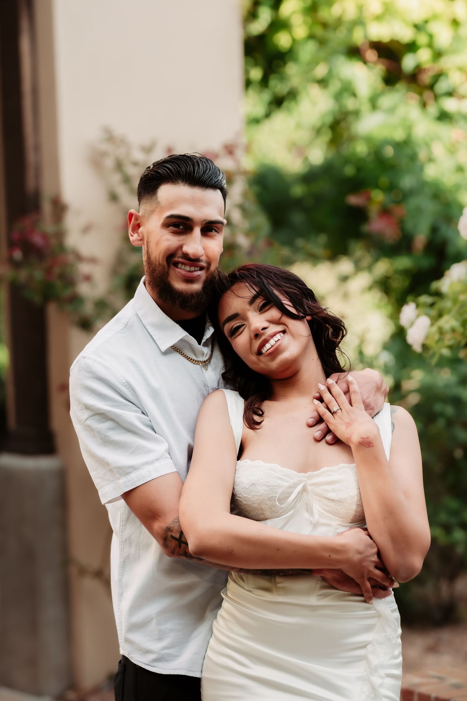 Happy couple embraces outdoors in romantic wedding photoshoot with lush greenery in background.