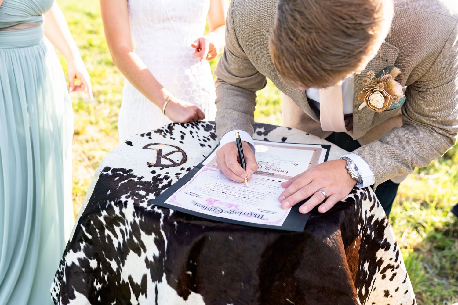 Hands signing a marriage certificate on a decorative black and white patterned tablecloth.