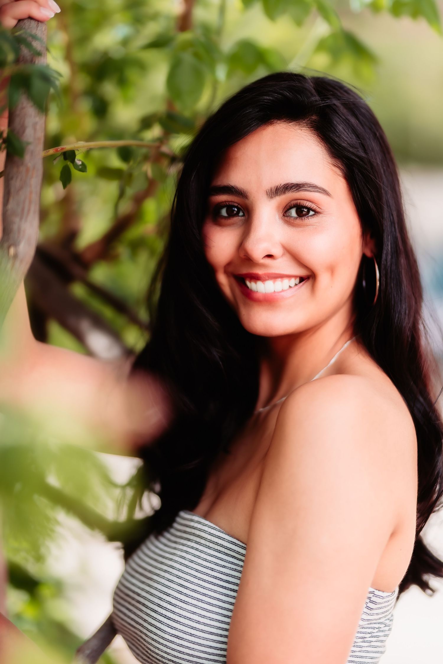 A portrait in nature wearing a striped top with green foliage in the background.