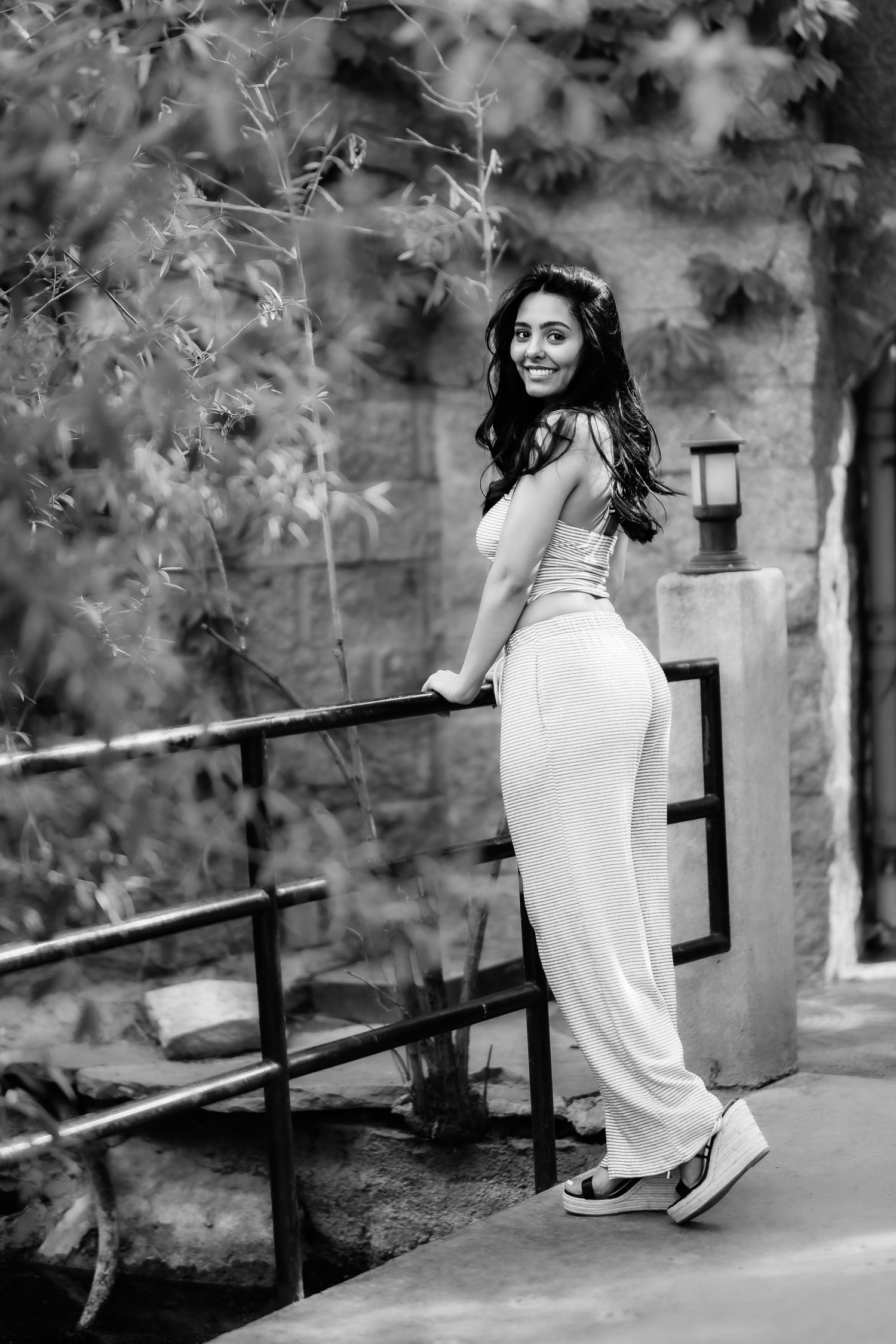 Black and white portrait of someone in fitted outfit posing elegantly on outdoor steps.