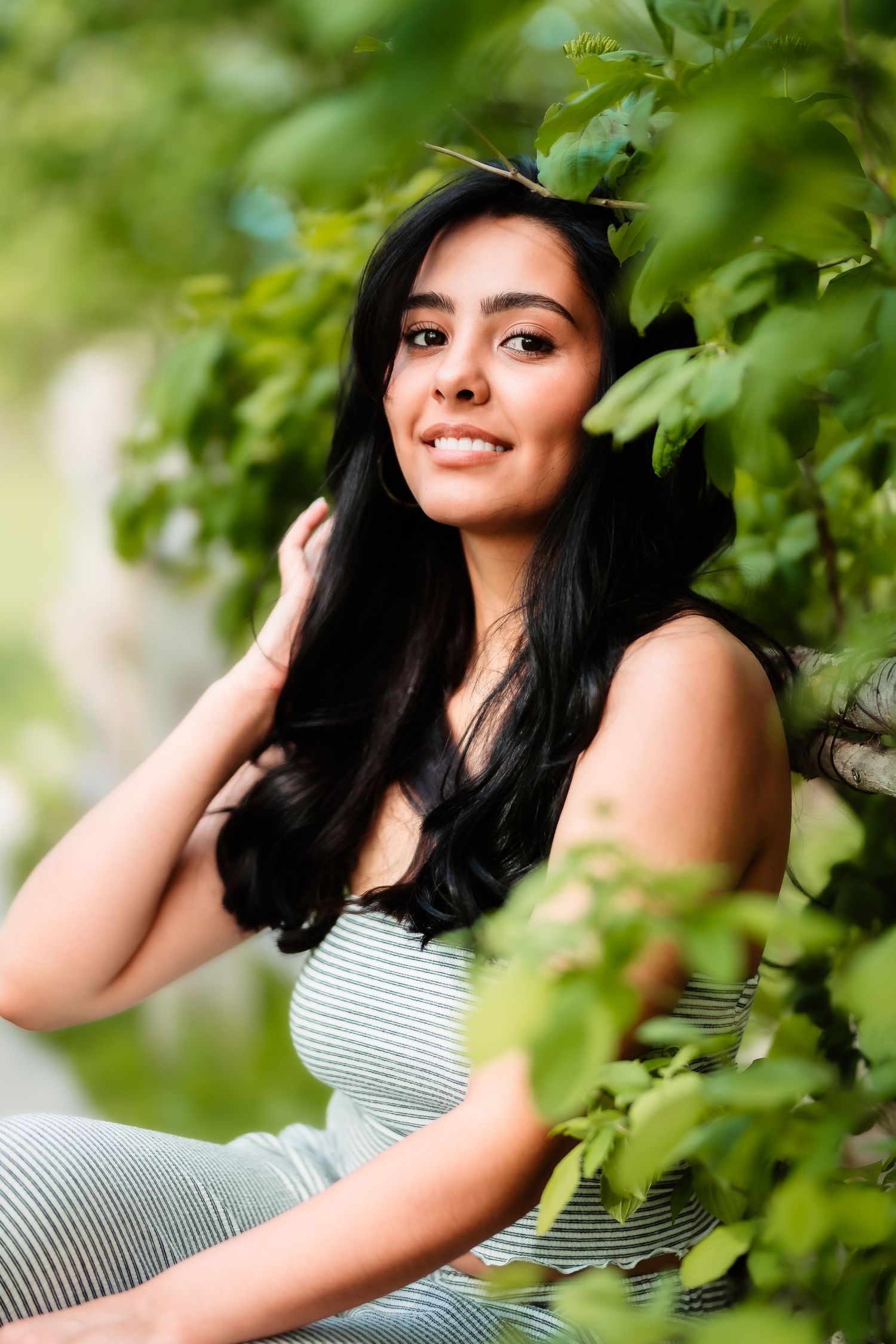 Natural outdoor portrait framed by green leaves in striped summer outfit.