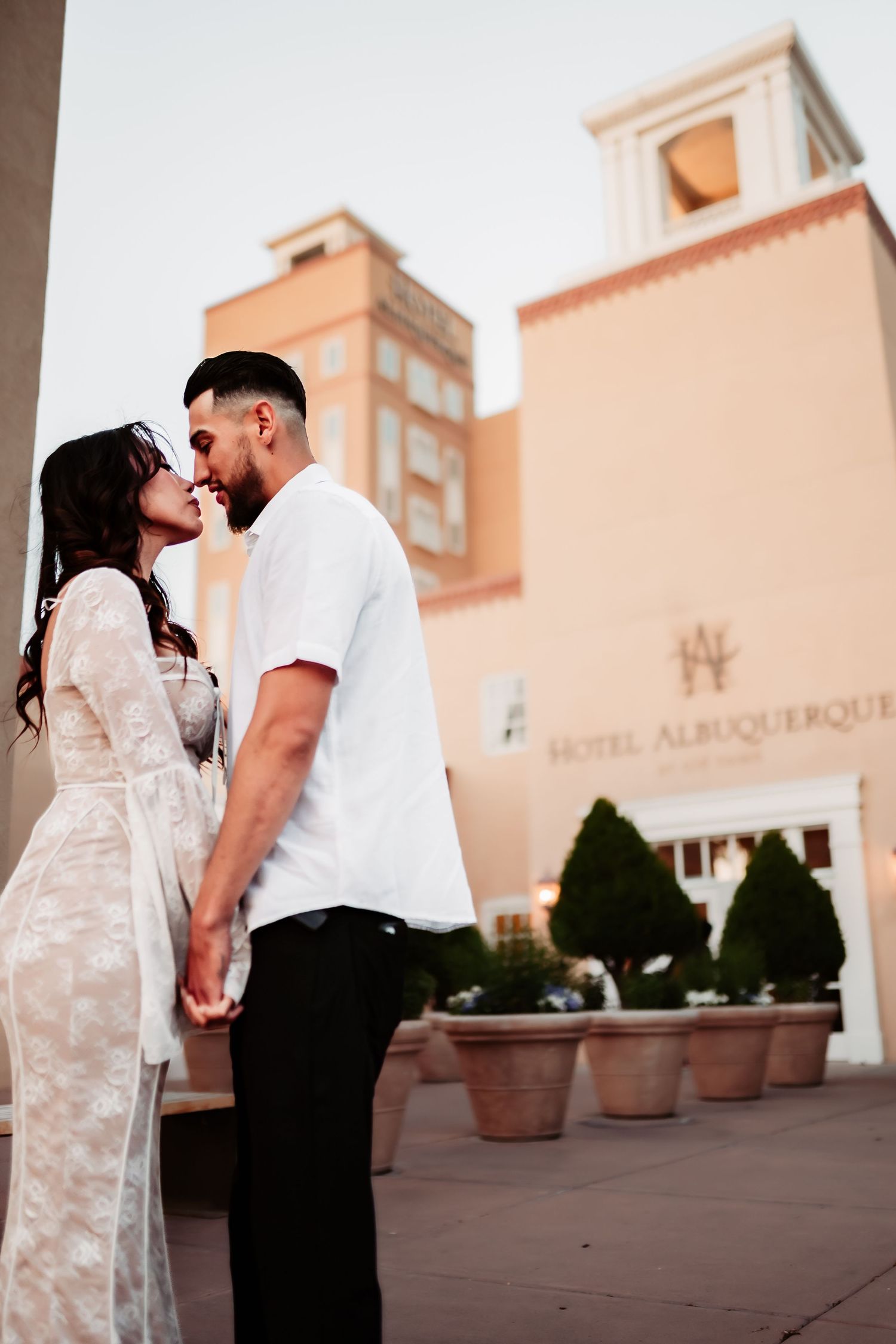 Romantic couple sharing an intimate moment outside Hotel Albuquerque with Spanish-style architecture in background.