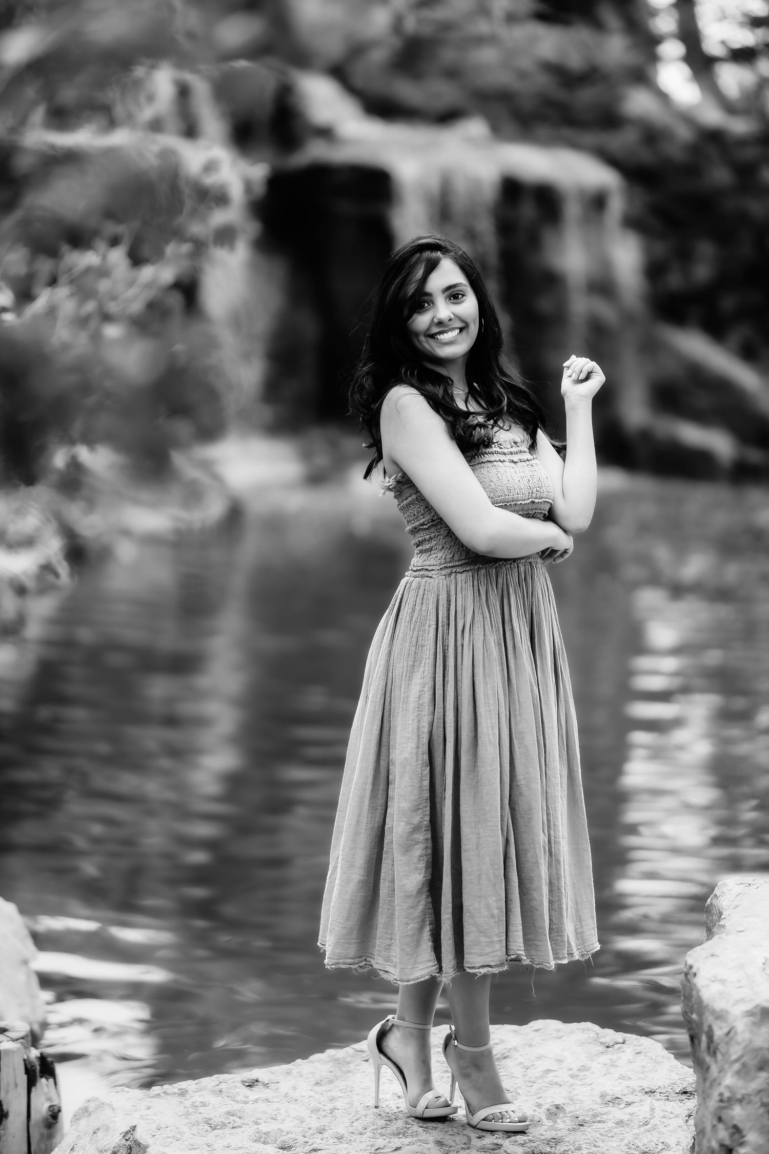 A black and white portrait of a woman in a flowing dress standing by a waterfall.