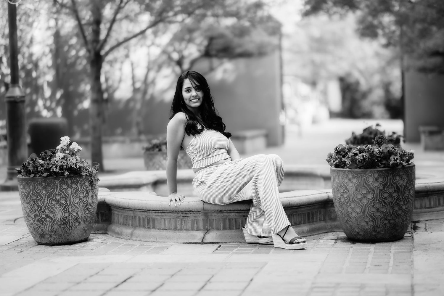 Black and white photo of someone sitting gracefully between decorative planters in an outdoor setting.
